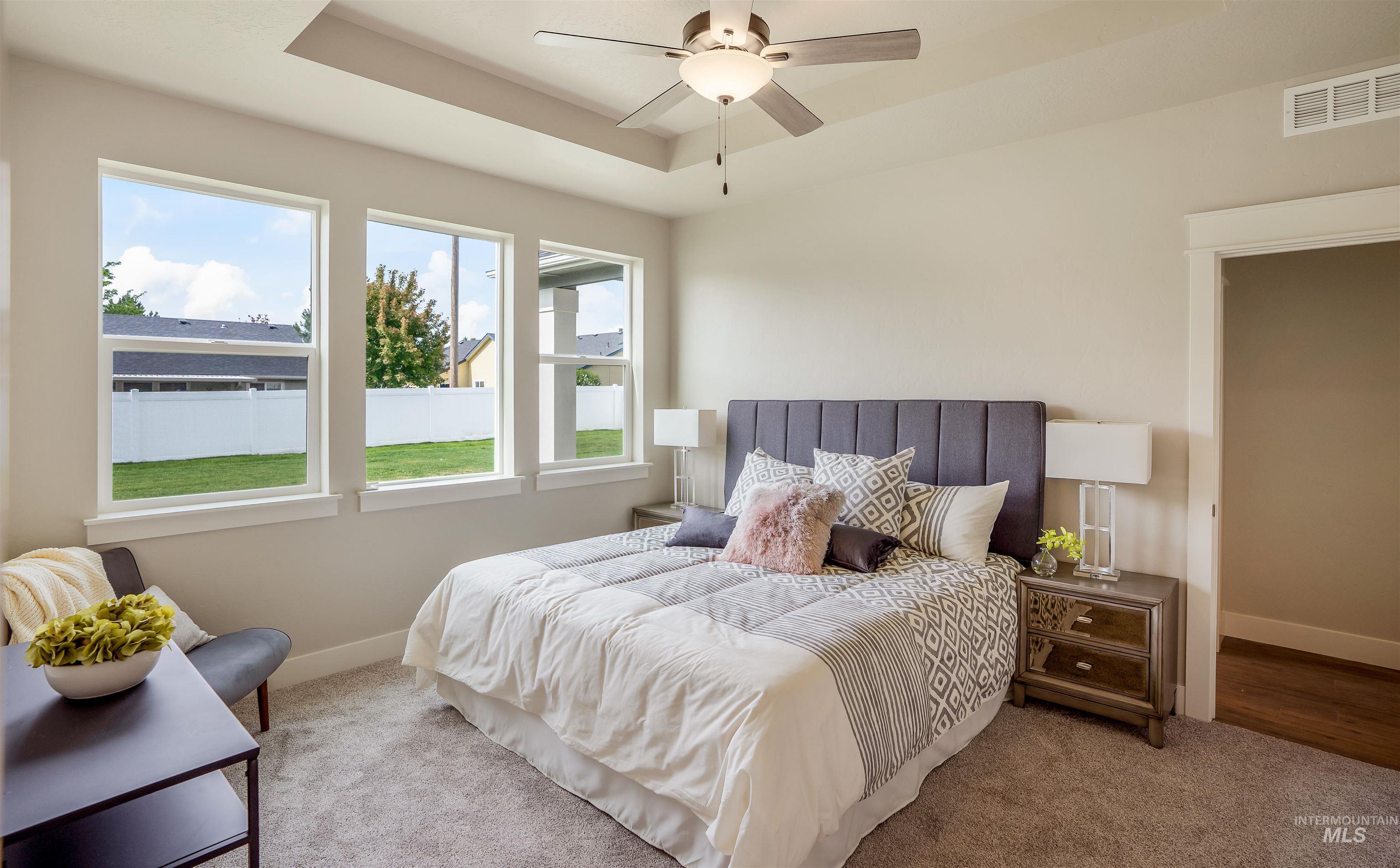 Carpeted bedroom featuring a tray ceiling and ceiling fan