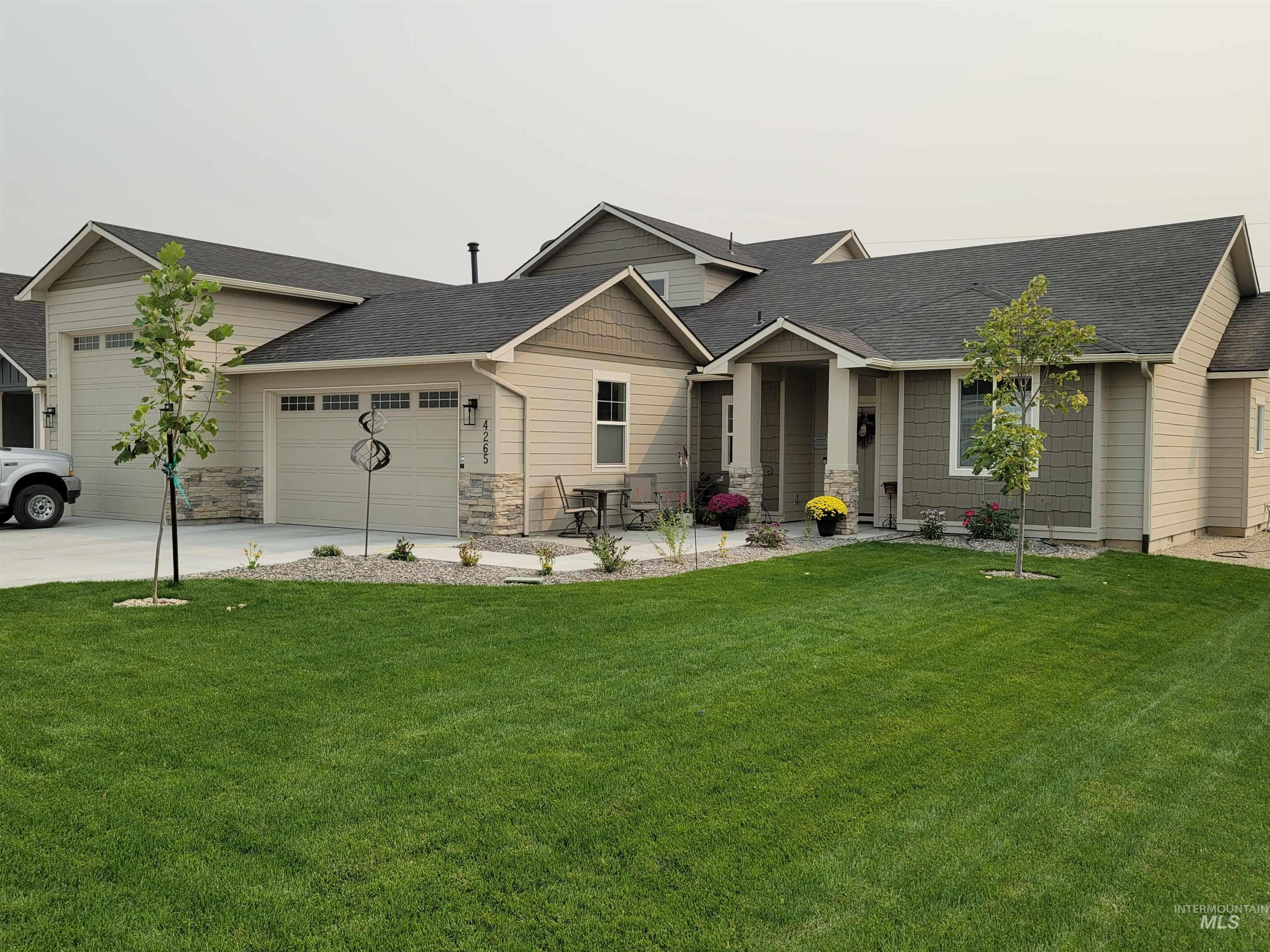View of front of house featuring a shingled roof, a front yard, an attached garage, driveway, and stone siding