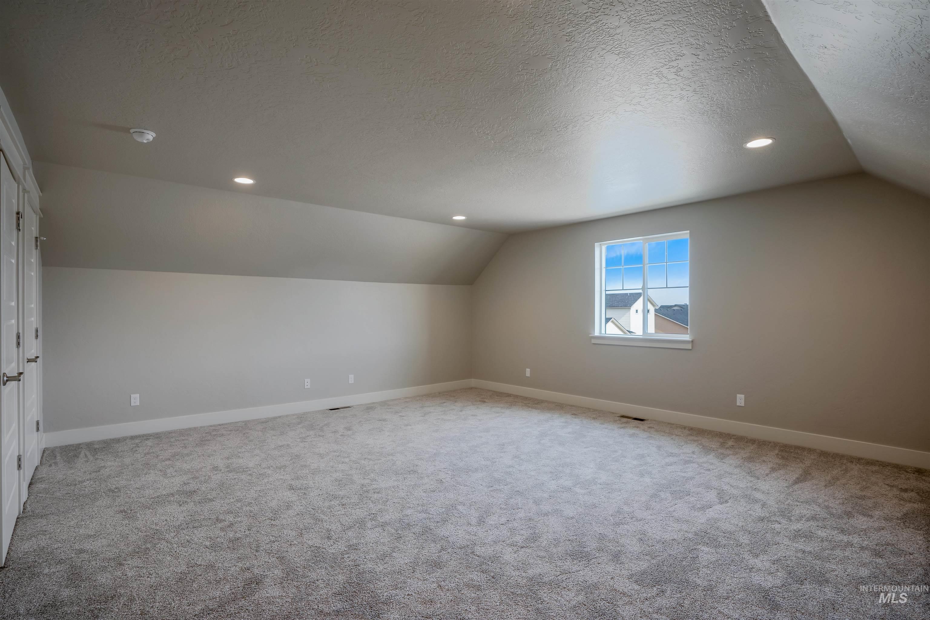 Bonus room featuring a textured ceiling, lofted ceiling, recessed lighting, and light colored carpet