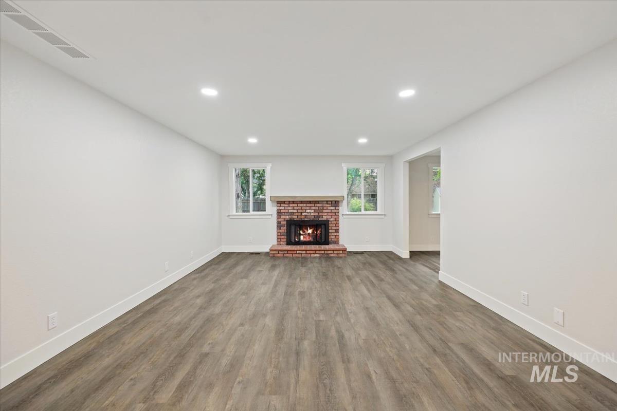 Unfurnished living room with recessed lighting, a brick fireplace, and dark wood-style flooring