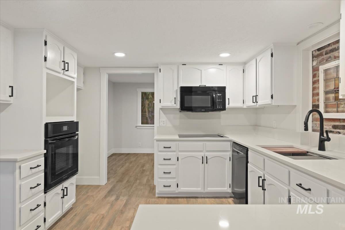 Kitchen featuring white cabinets, black appliances, light wood-style flooring, recessed lighting, and light stone countertops