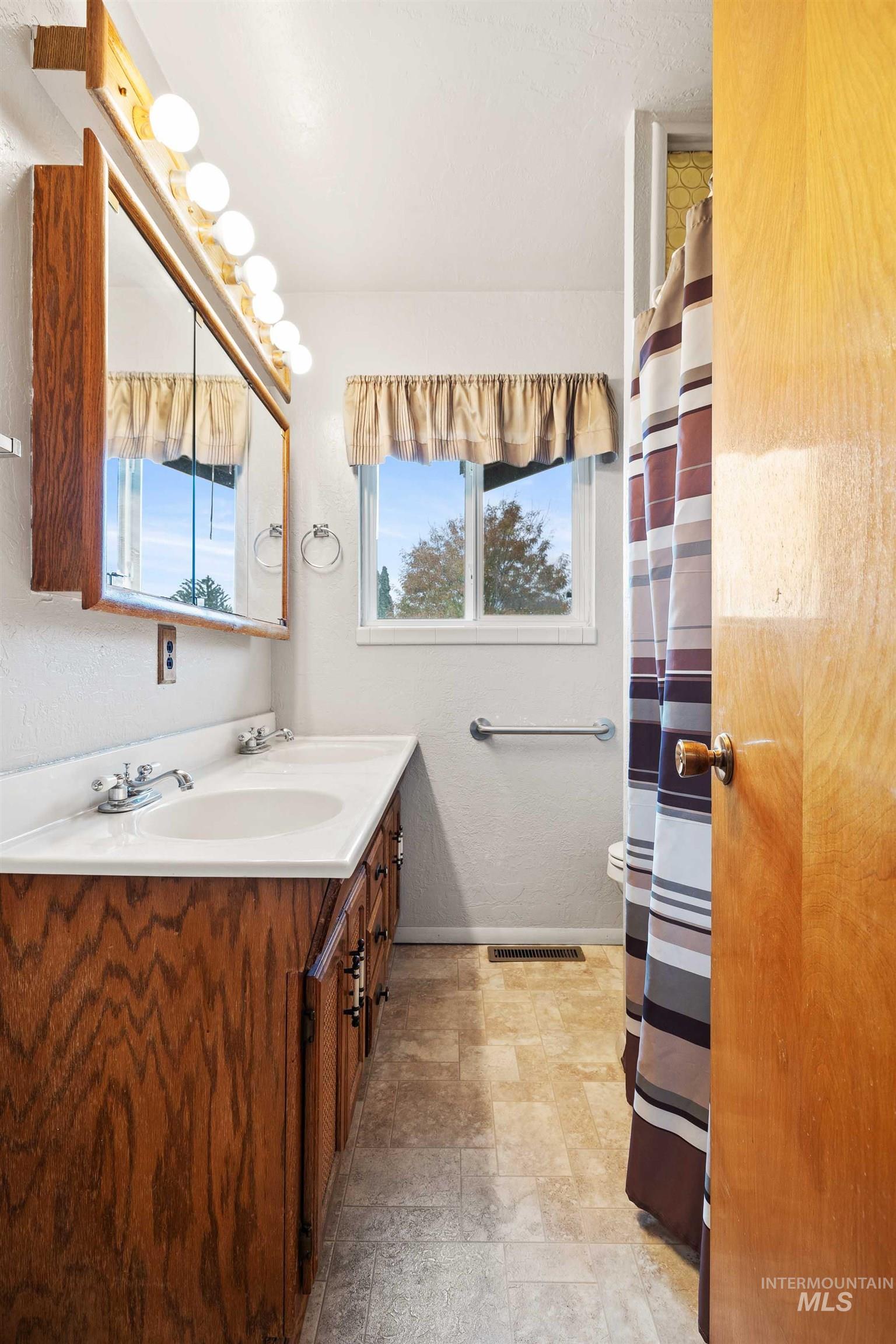 Full bathroom with double vanity, a shower with shower curtain, and a textured wall