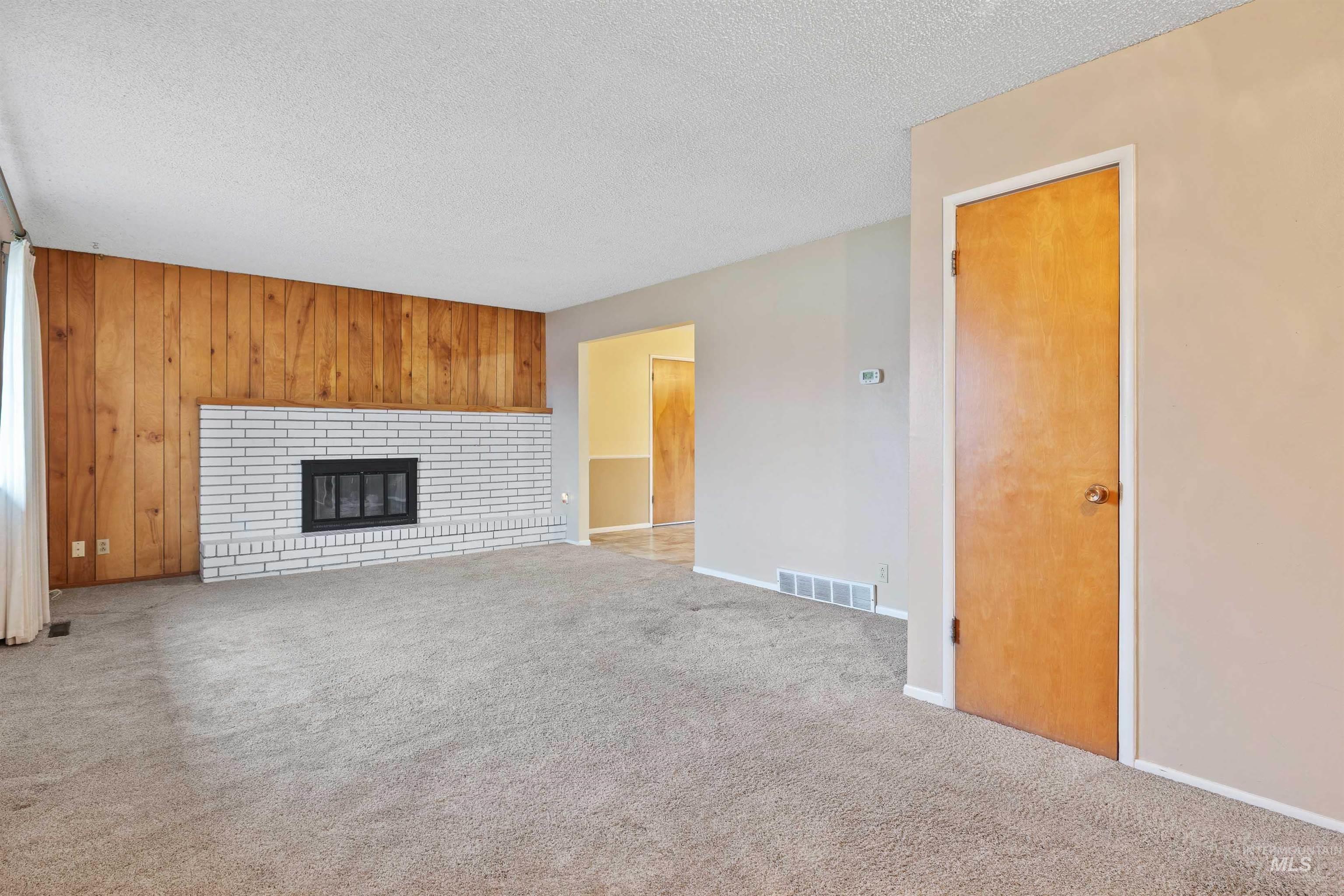 Unfurnished living room with wood walls, a textured ceiling, carpet floors, and a brick fireplace
