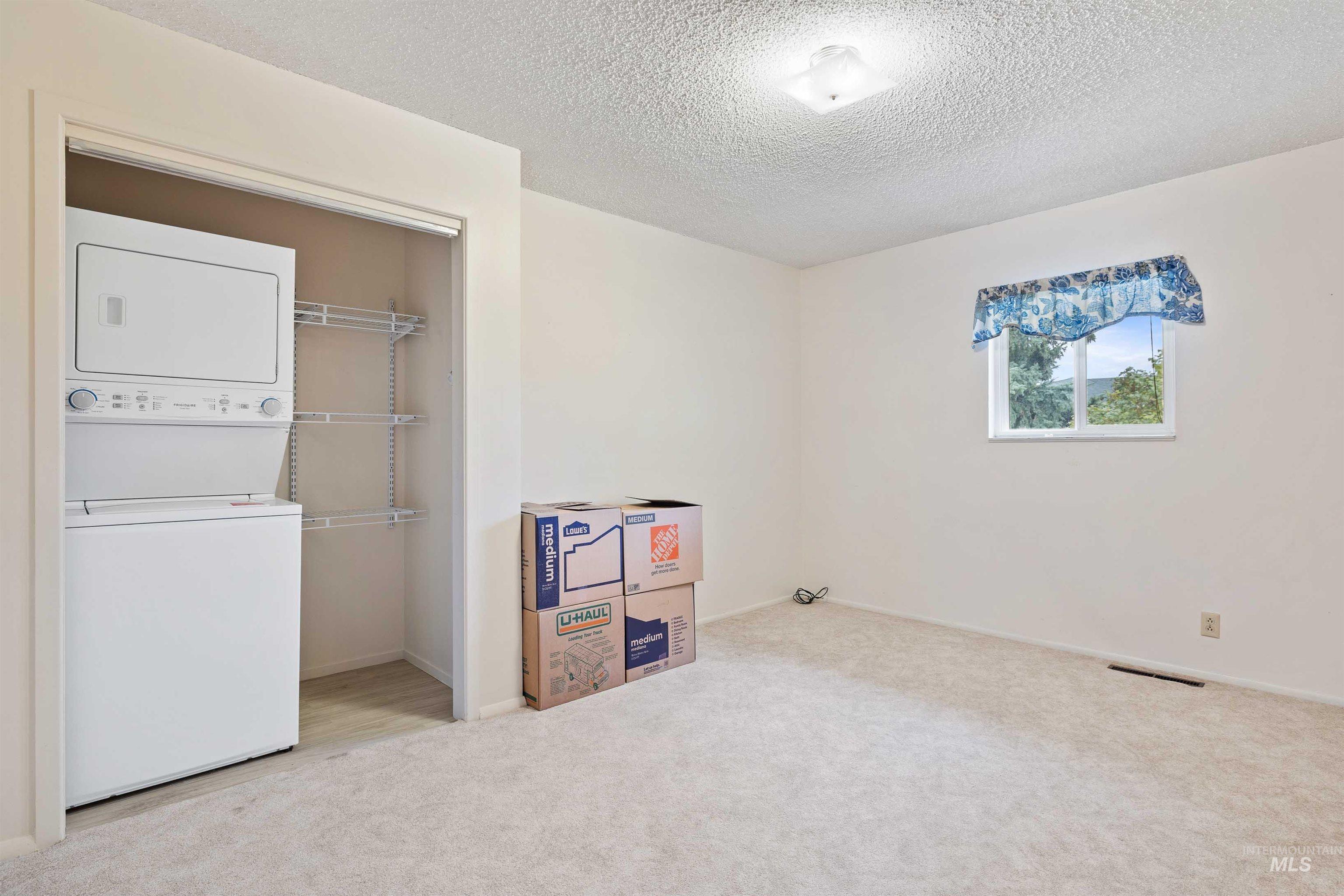 Laundry room featuring light carpet, estacked washer and dryer, and a textured ceiling