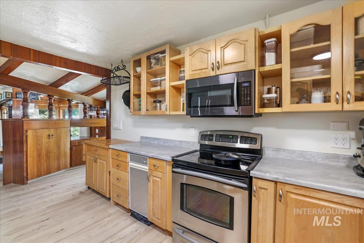 Kitchen with appliances with stainless steel finishes, open shelves, light wood finished floors, light countertops, and a textured ceiling