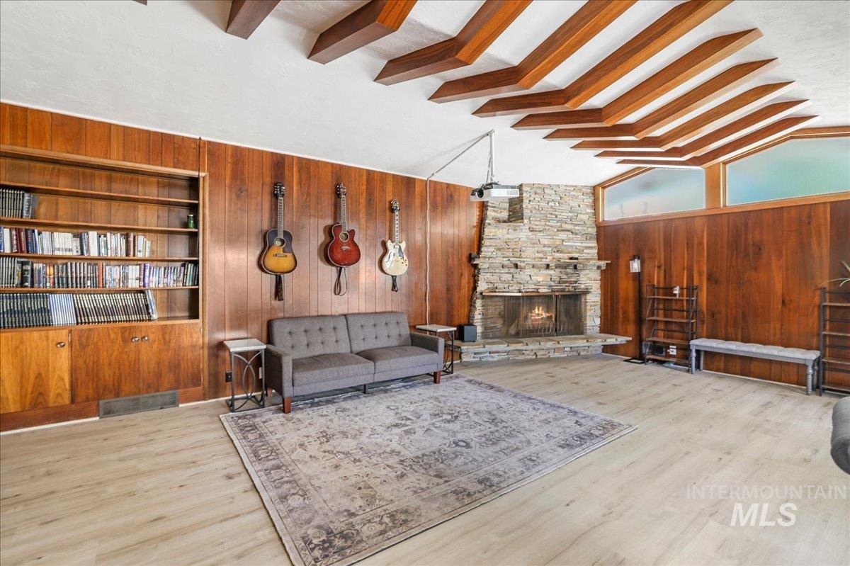 Living room featuring wood walls, beam ceiling, built in features, a fireplace, and wood finished floors