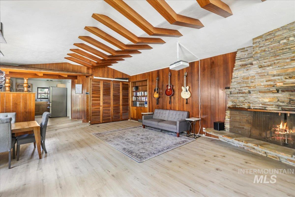 Living room with wood walls, lofted ceiling, wood finished floors, and a stone fireplace