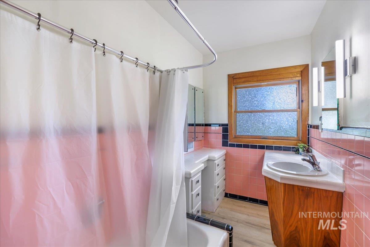 Full bathroom featuring vanity, tile walls, wood finished floors, and wainscoting