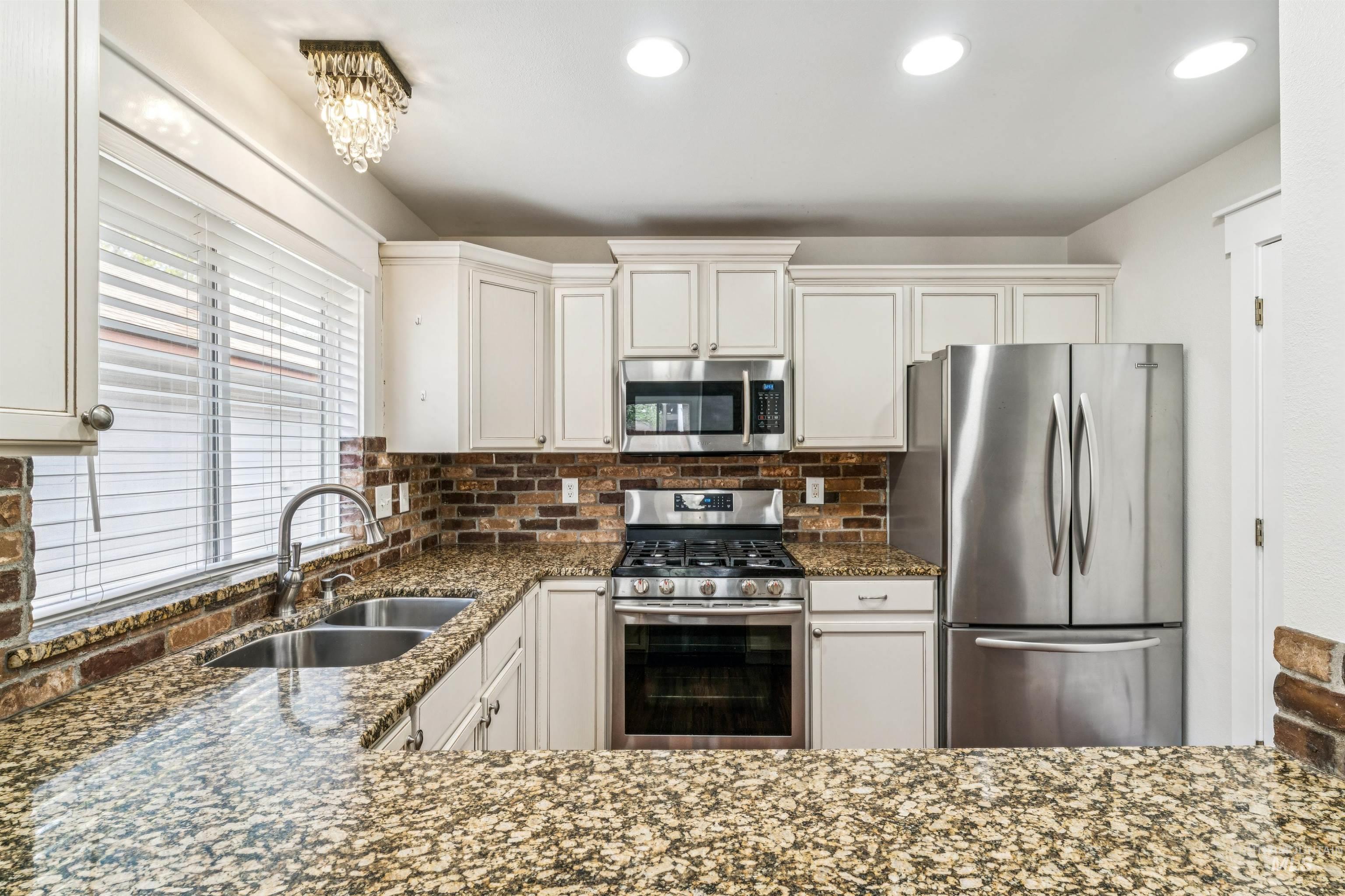 Kitchen with stainless steel appliances, dark stone counters, white cabinets, recessed lighting, and backsplash