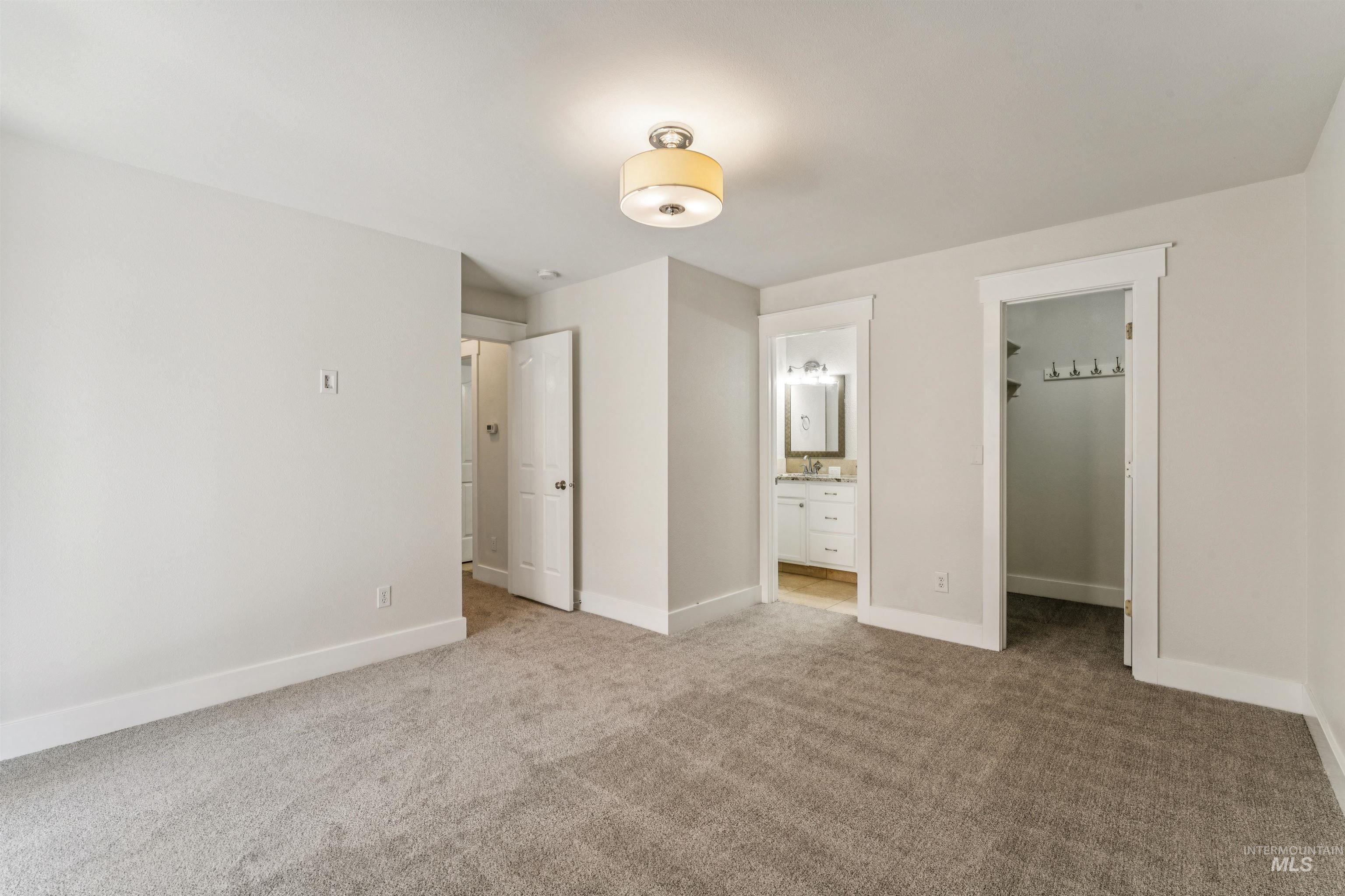 Unfurnished bedroom with a spacious closet, light carpet, and ensuite bath