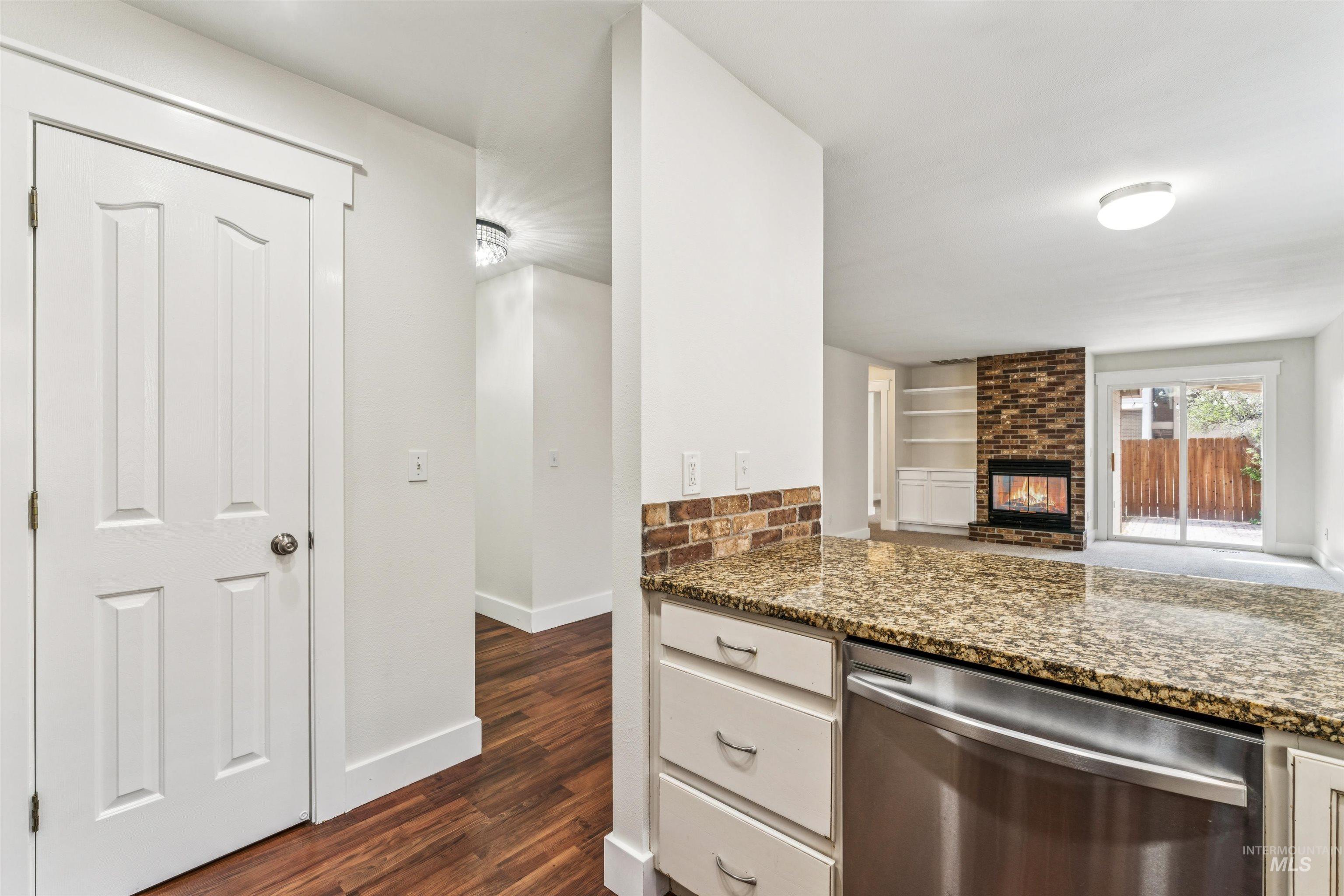 Kitchen with dishwasher, a multi sided fireplace, dark wood finished floors, light stone countertops, and open floor plan