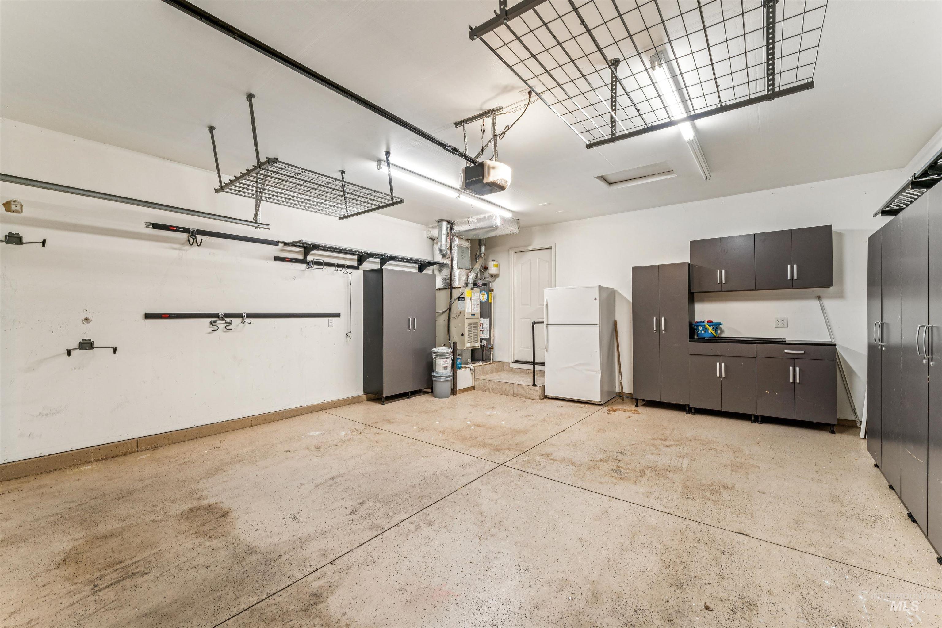 Garage with freestanding refrigerator, a garage door opener, and heating unit