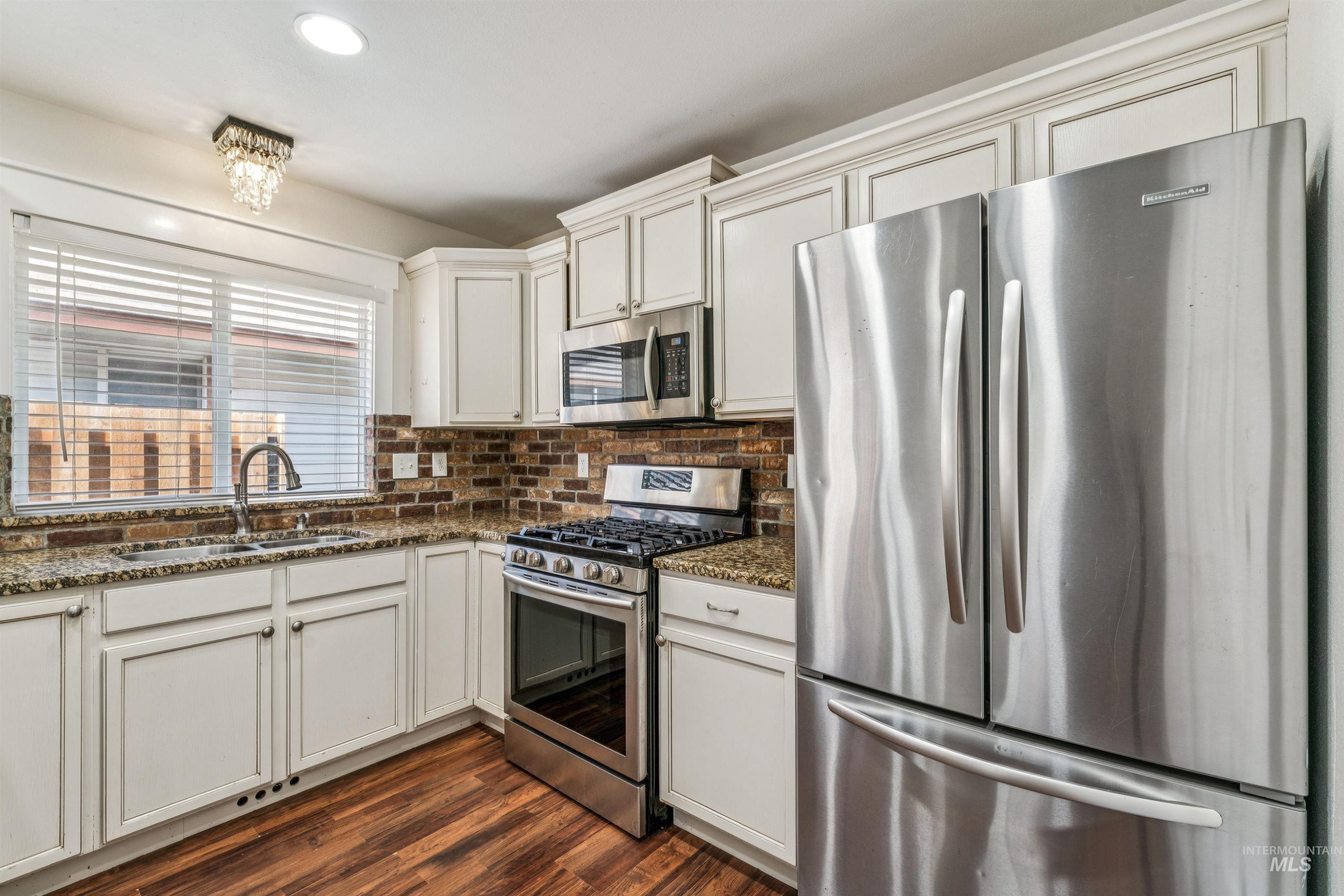 Kitchen with stainless steel appliances, dark wood finished floors, dark stone countertops, white cabinetry, and recessed lighting