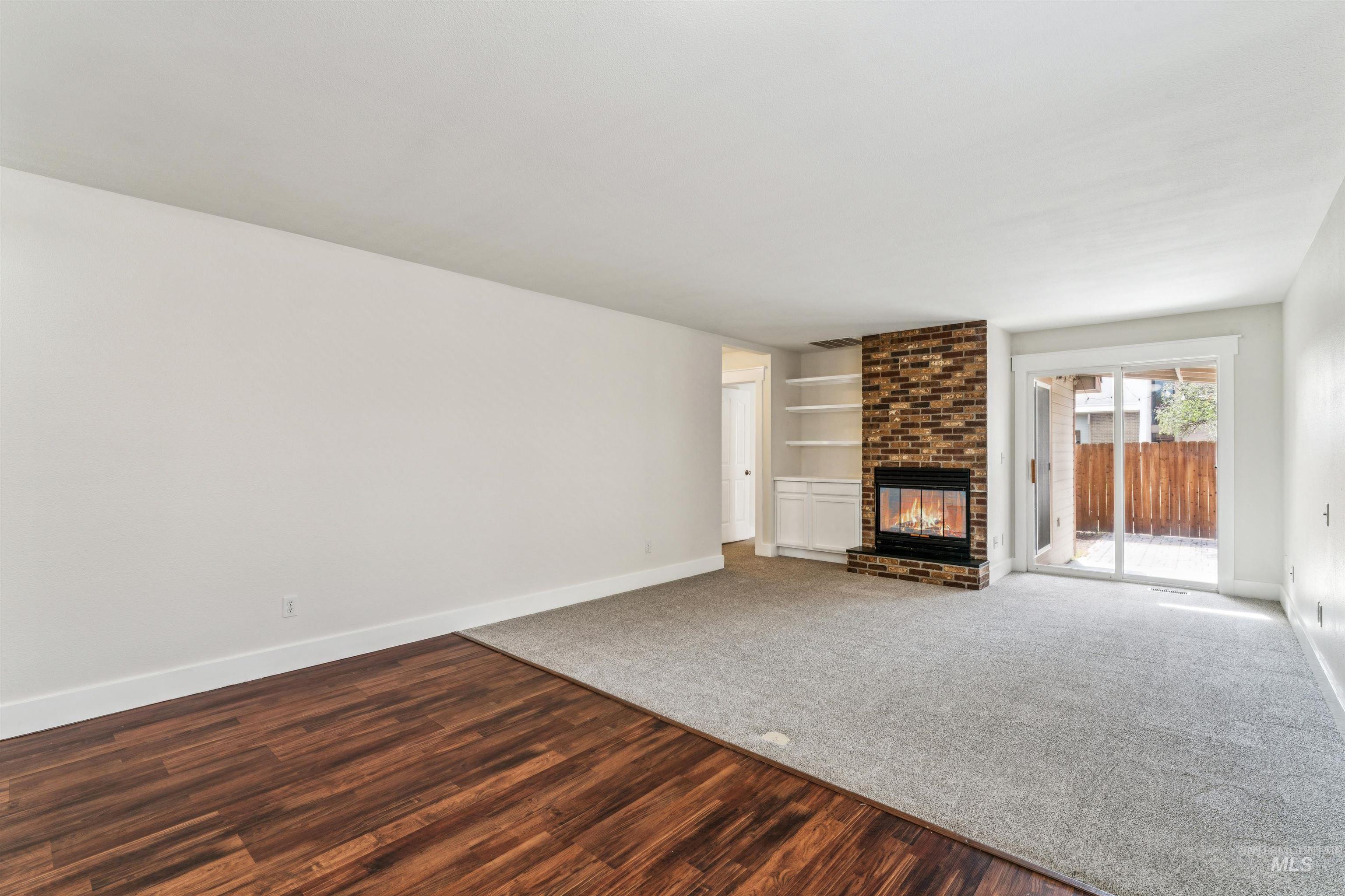 Unfurnished living room with built in features, dark wood-style flooring, and a brick fireplace