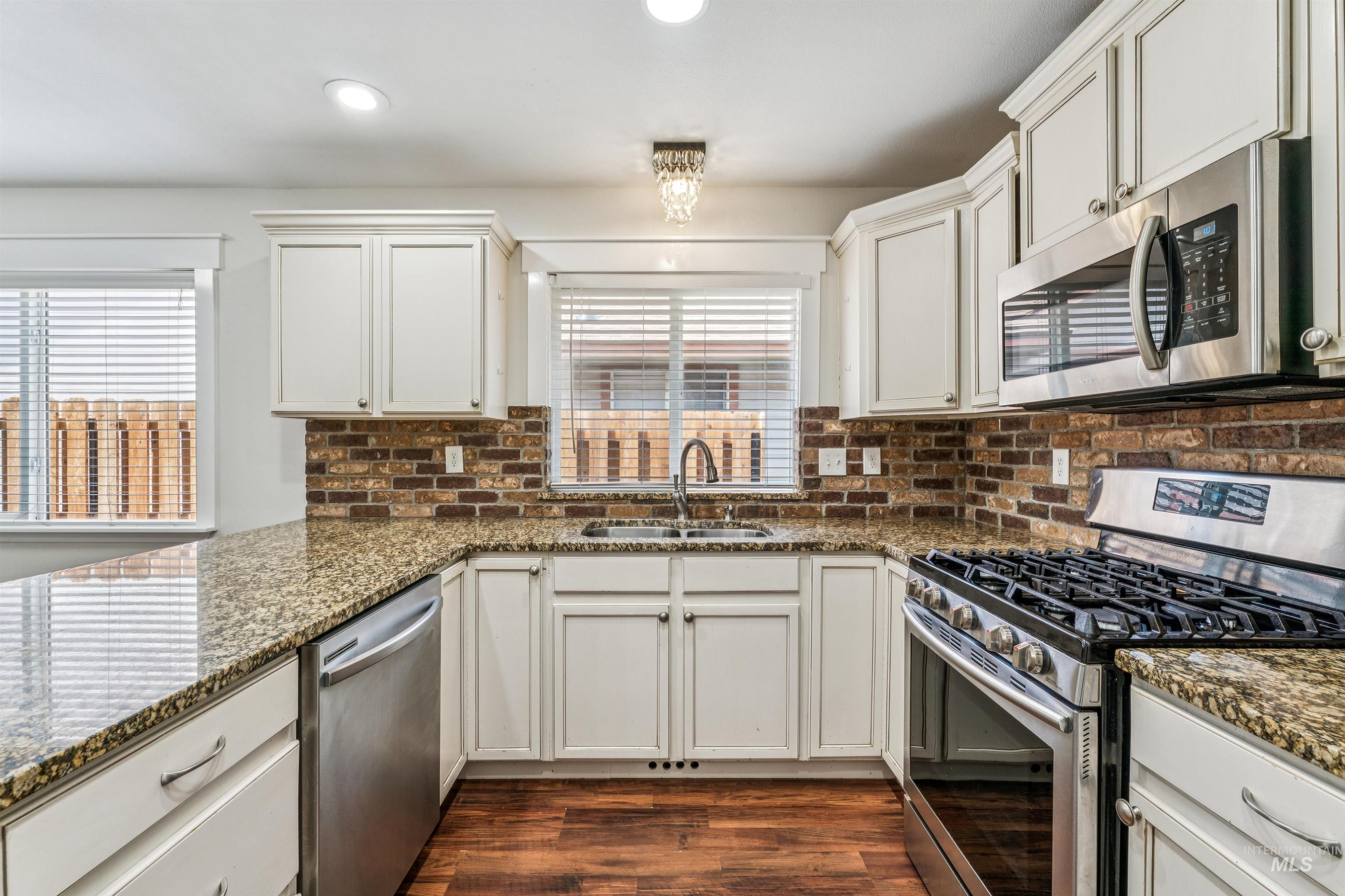 Kitchen featuring stainless steel appliances, dark stone countertops, white cabinetry, dark wood-type flooring, and recessed lighting