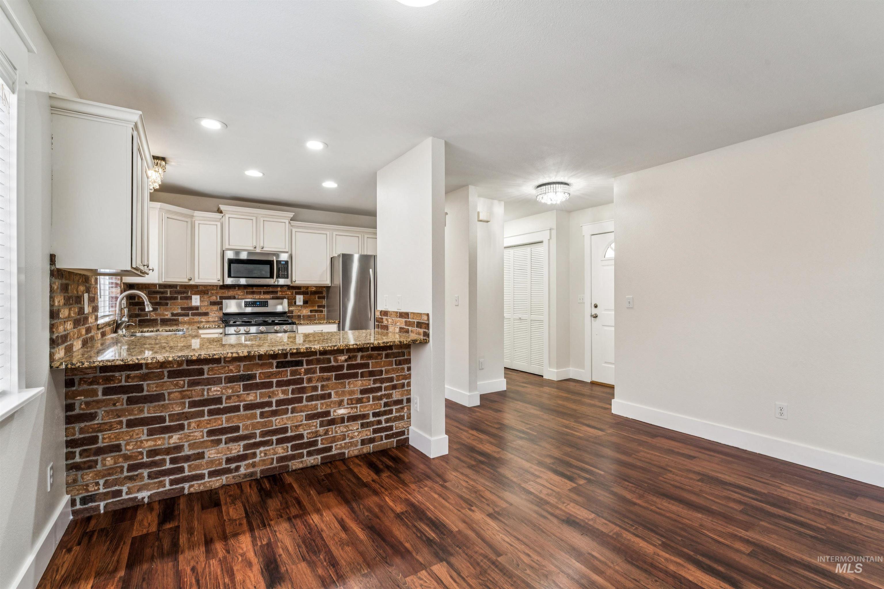 Kitchen featuring light stone counters, stainless steel appliances, white cabinetry, dark wood finished floors, and recessed lighting