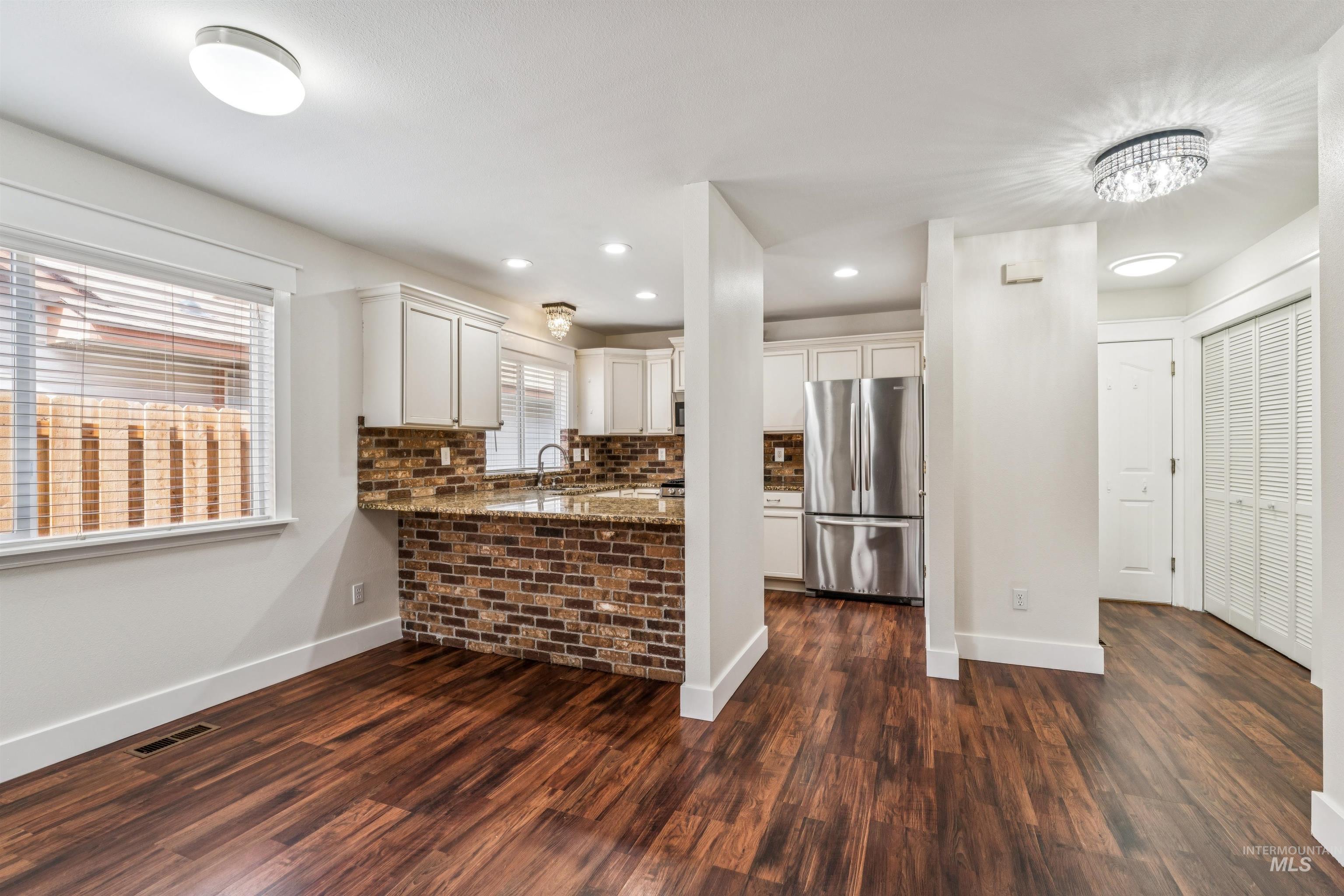 Kitchen featuring freestanding refrigerator, dark stone counters, white cabinets, dark wood-style floors, and a peninsula