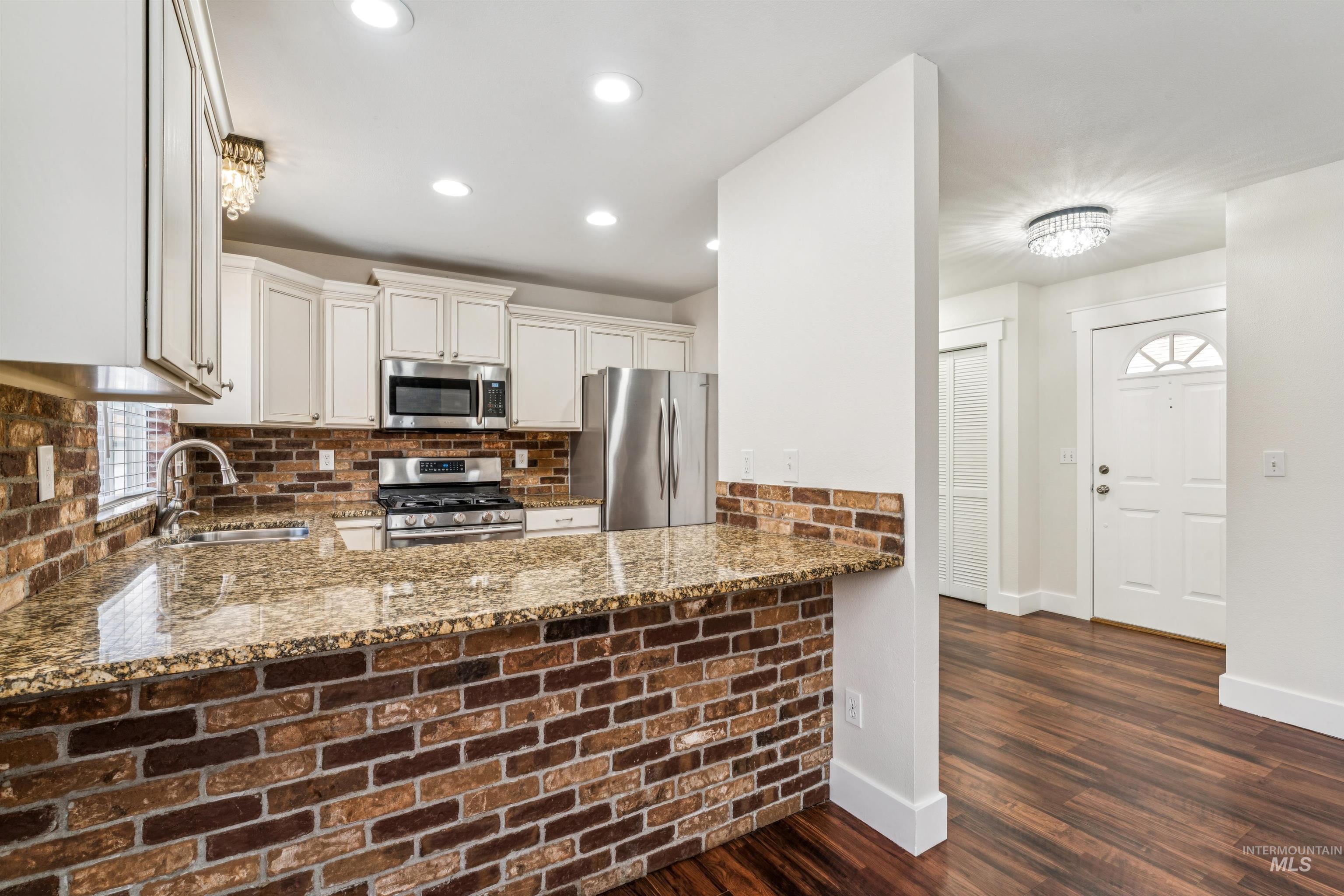 Kitchen featuring dark stone counters, stainless steel appliances, dark wood-type flooring, white cabinetry, and tasteful backsplash
