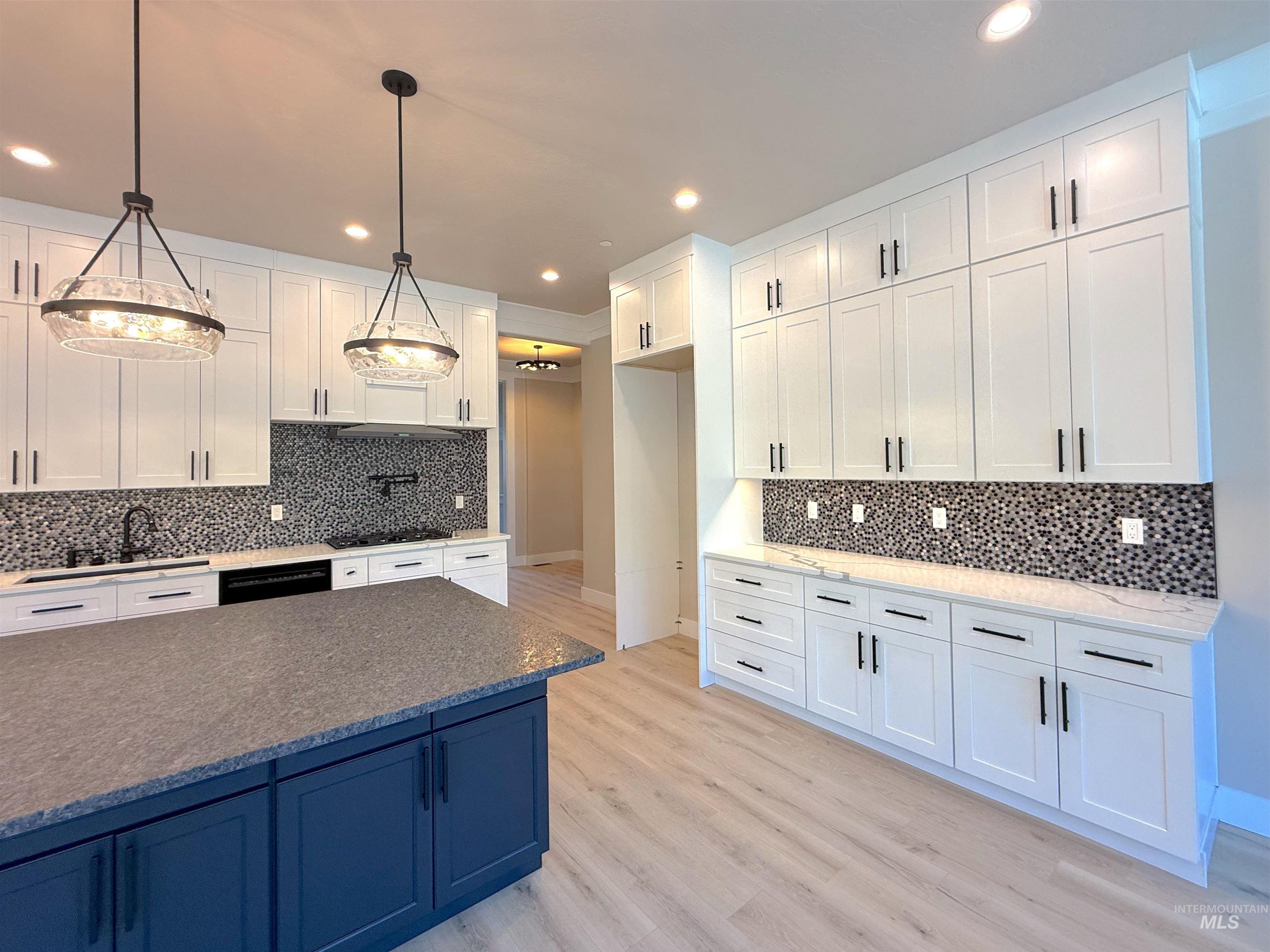 Kitchen featuring white cabinets, light stone counters, decorative backsplash, light wood-style flooring, and recessed lighting