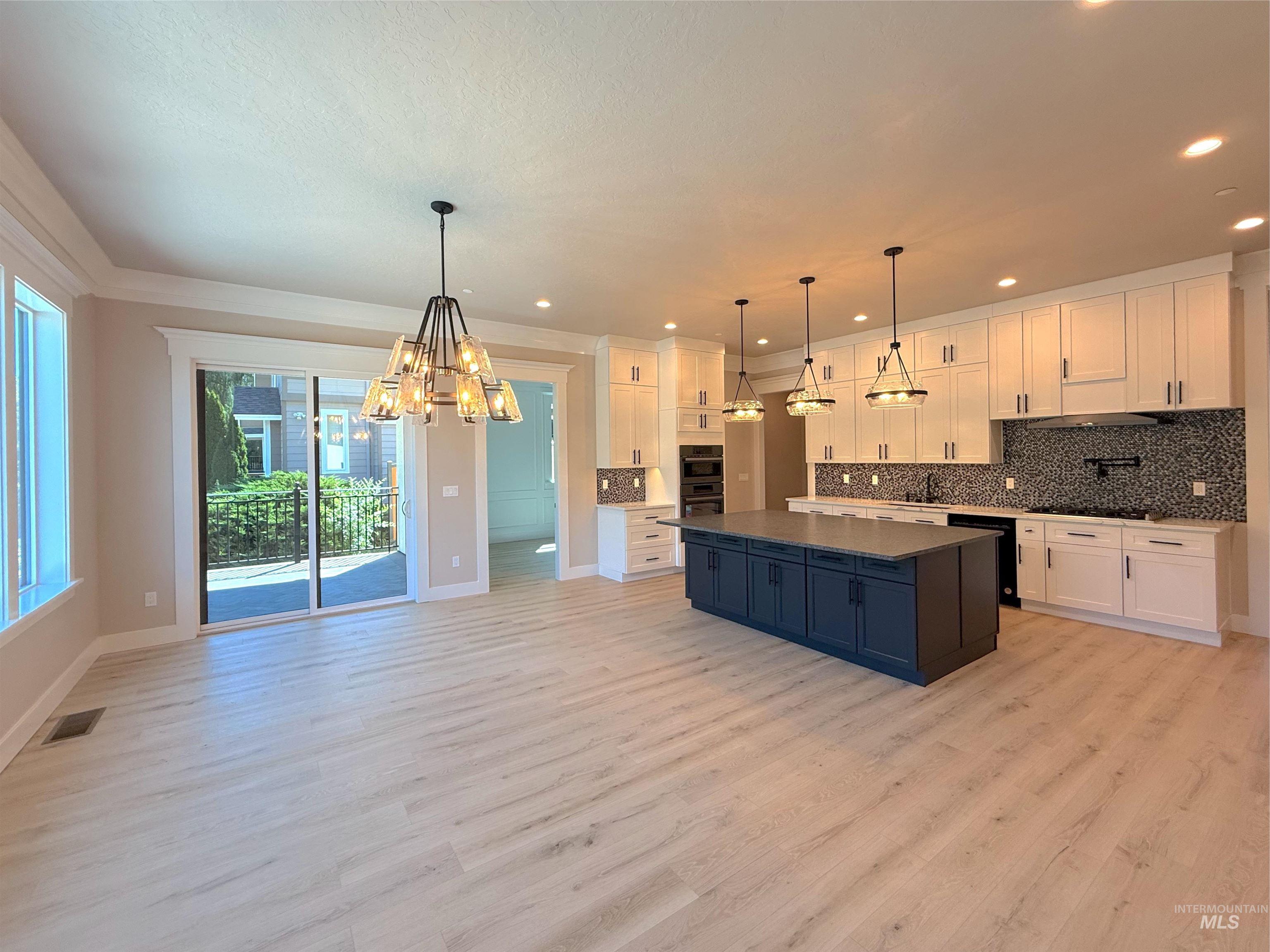 Kitchen featuring white cabinetry, backsplash, a chandelier, decorative light fixtures, and light wood finished floors