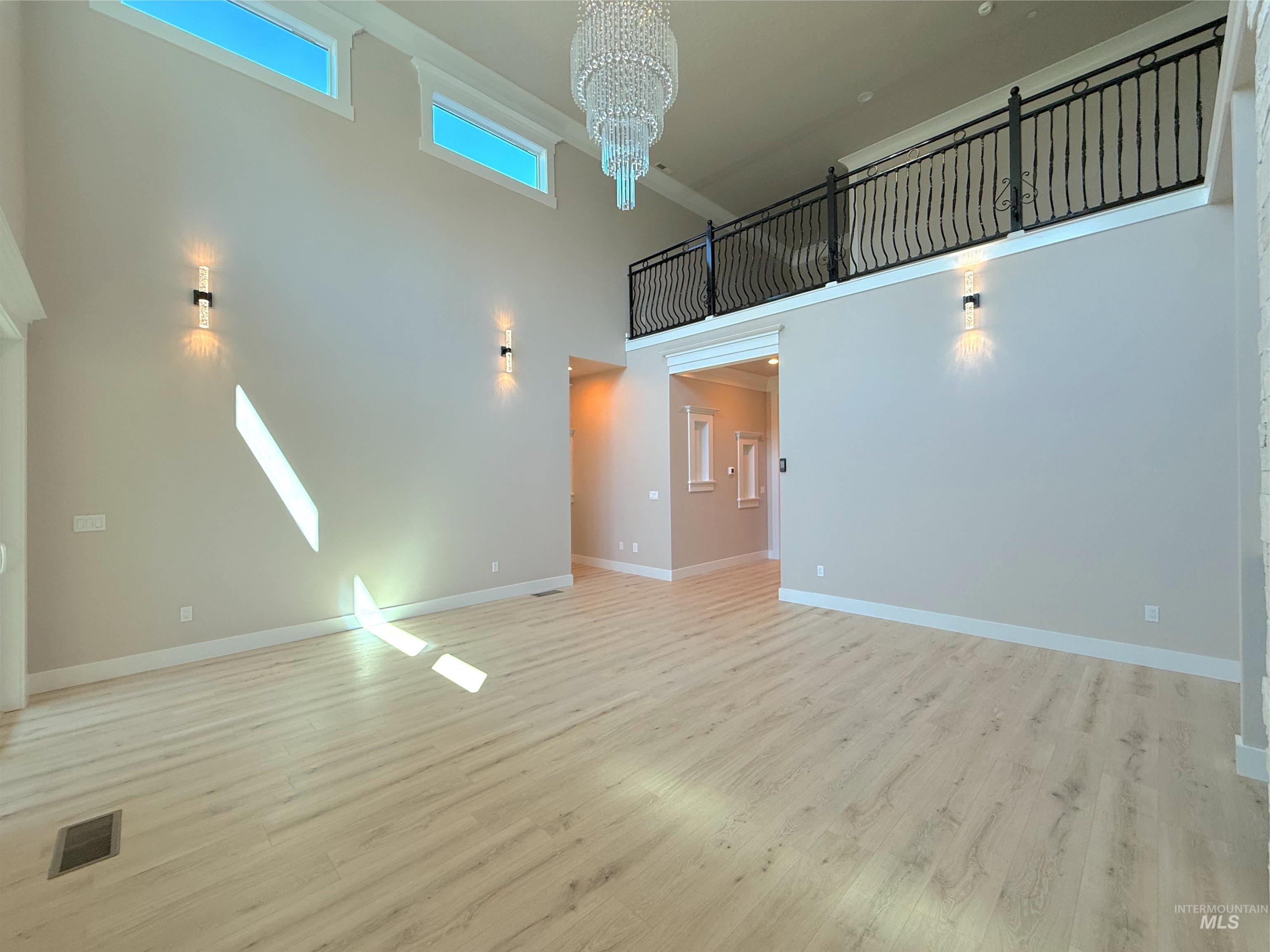 Unfurnished living room with a high ceiling, a chandelier, and light wood-type flooring