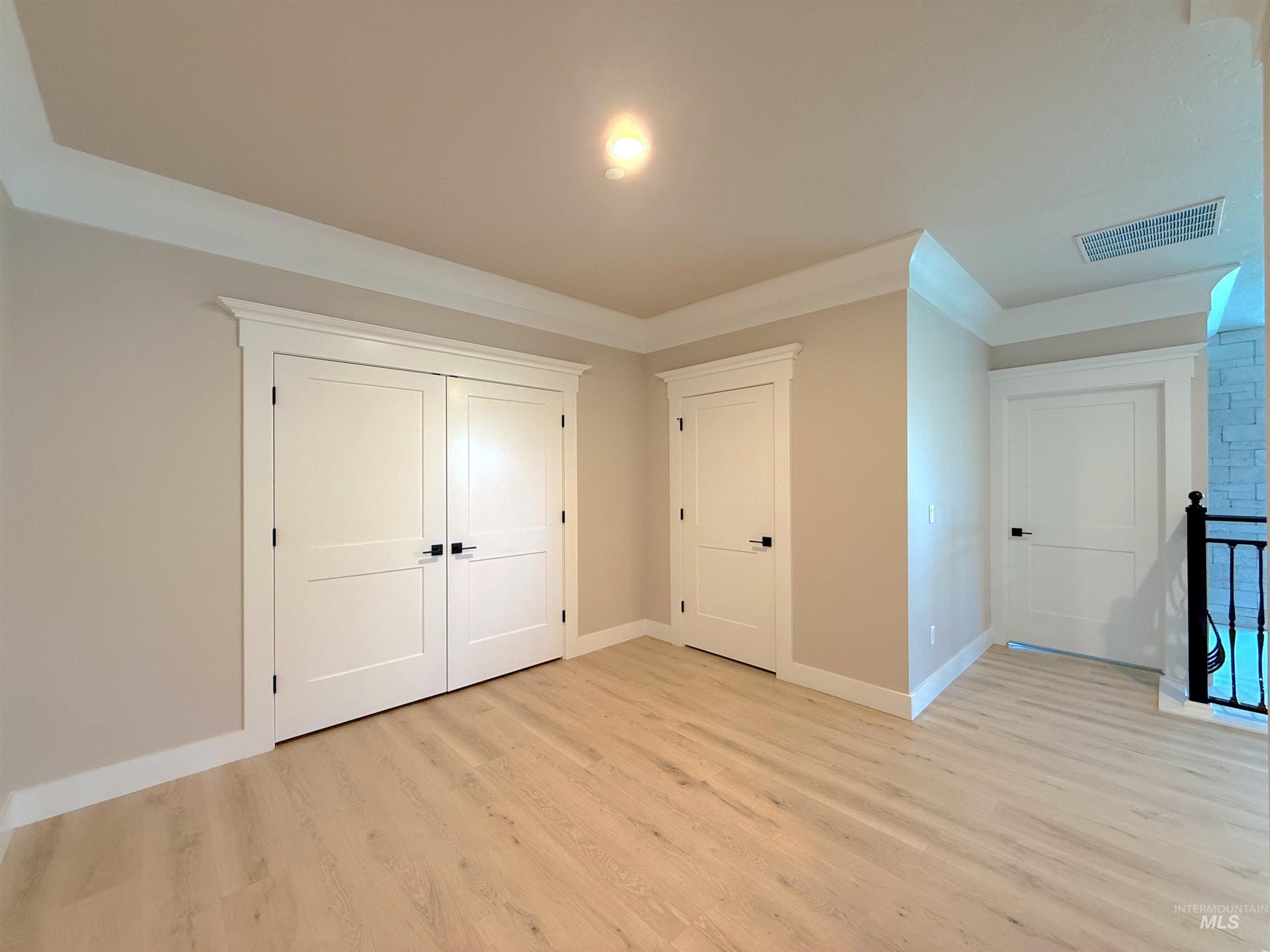 Unfurnished bedroom with light wood finished floors, crown molding, and a closet
