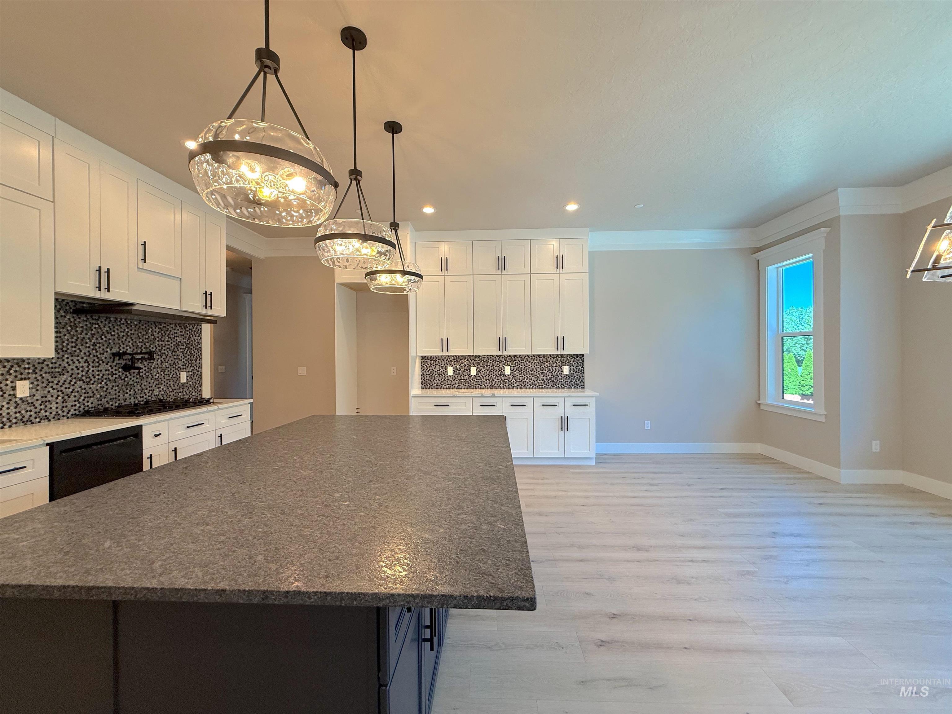Kitchen with dark stone countertops, white cabinetry, ornamental molding, a chandelier, and tasteful backsplash
