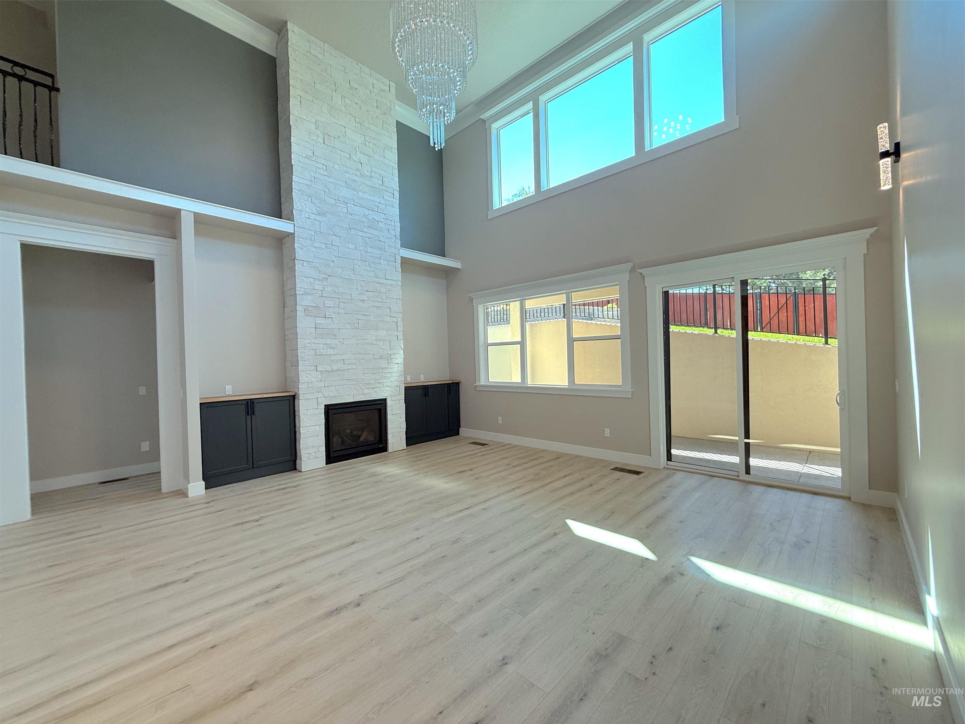 Unfurnished living room with a towering ceiling, light wood-type flooring, a fireplace, a chandelier, and ornamental molding