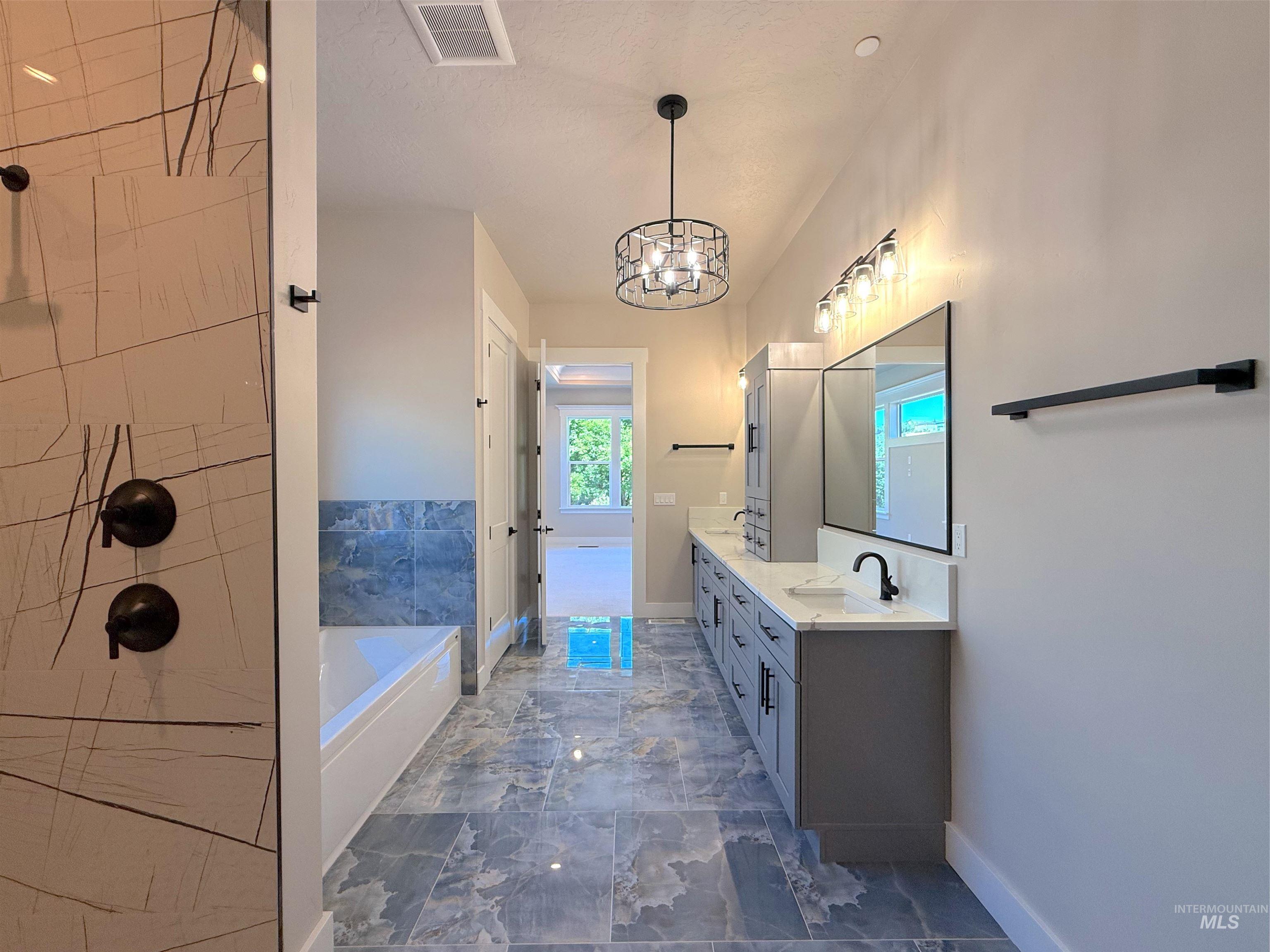Full bath featuring a bath, double vanity, a chandelier, and a tile shower