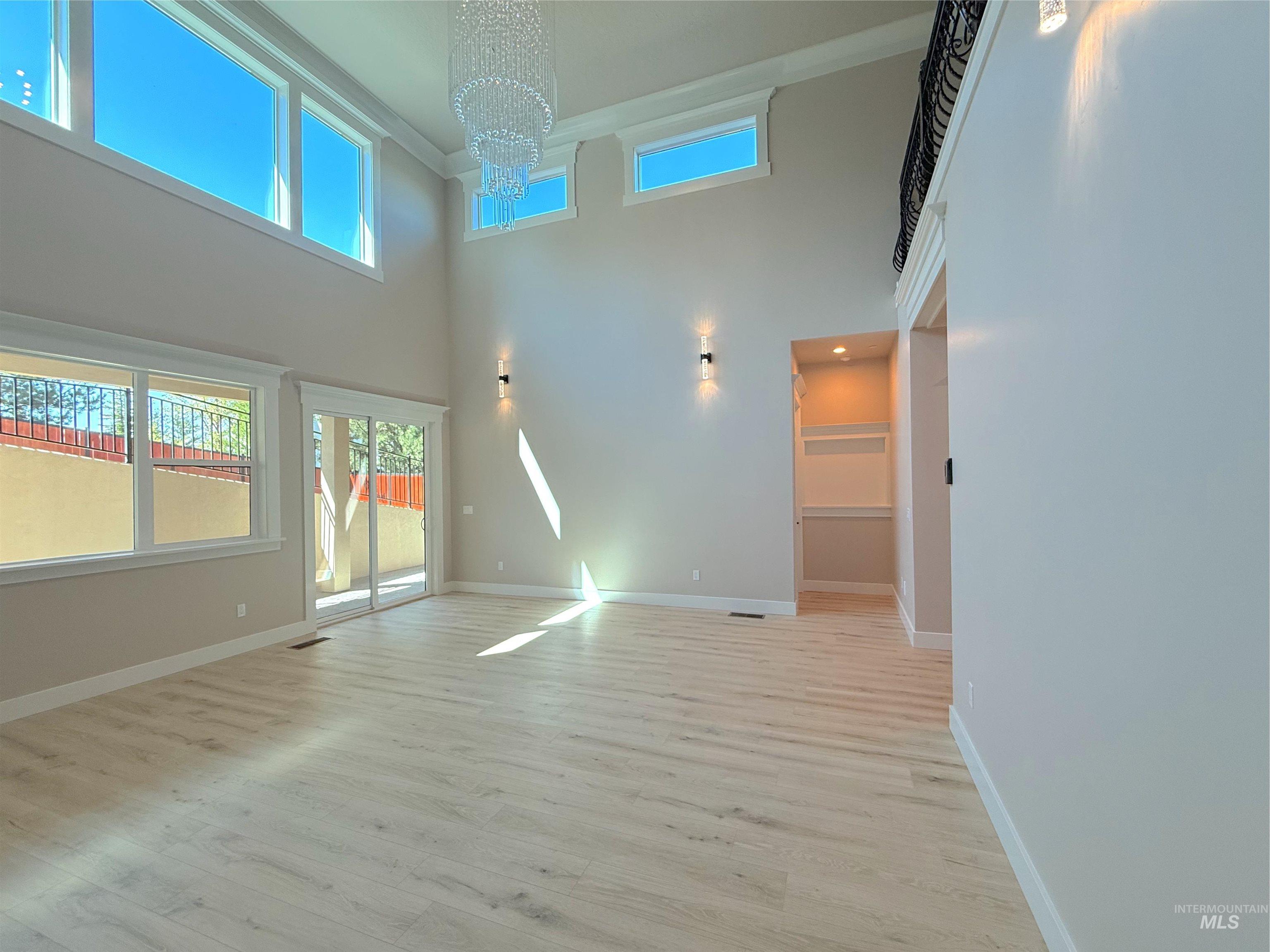 Unfurnished living room with light wood-type flooring, a high ceiling, a chandelier, plenty of natural light, and crown molding