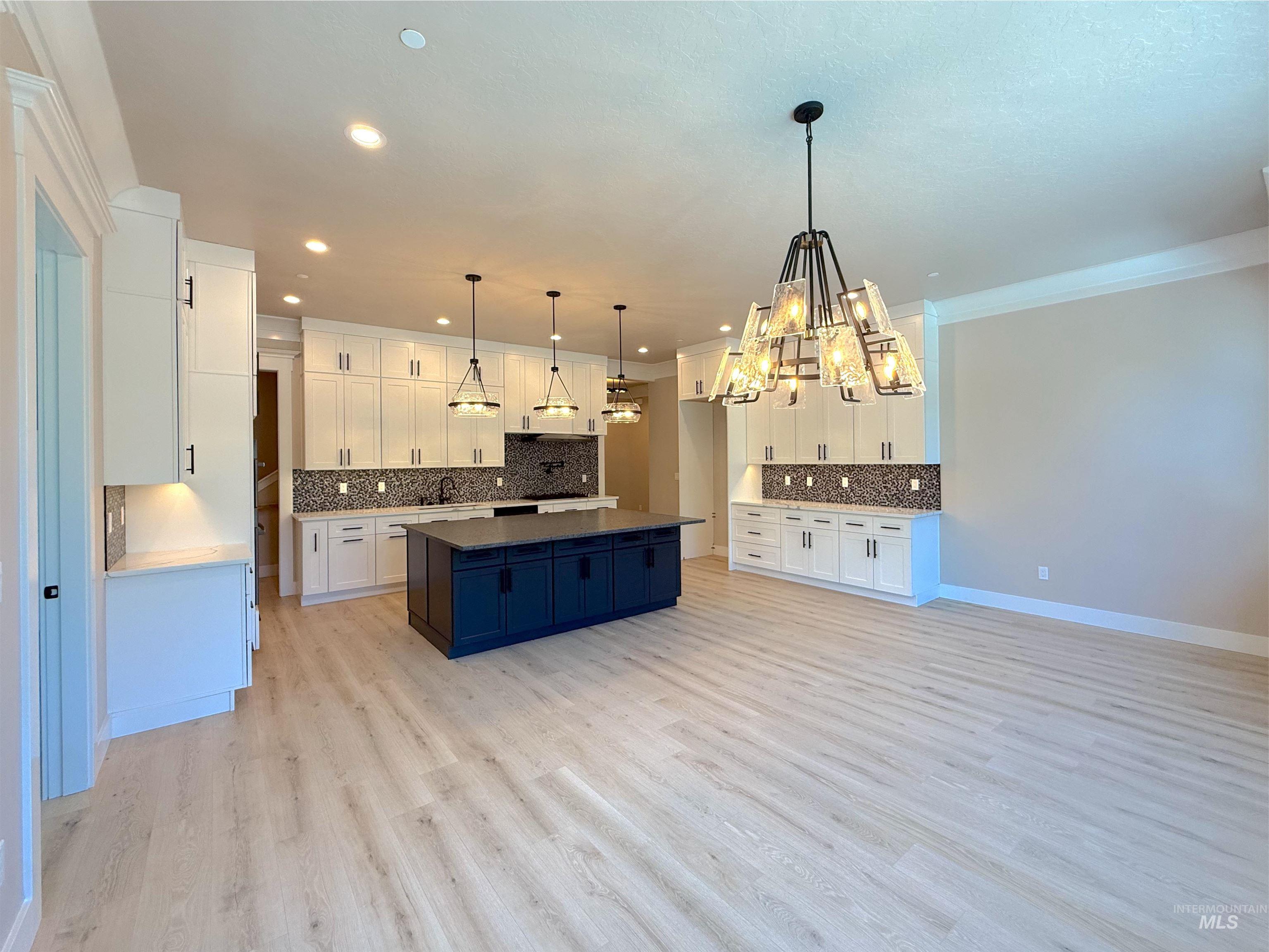 Kitchen featuring hanging light fixtures, white cabinetry, decorative backsplash, a chandelier, and light wood-style flooring