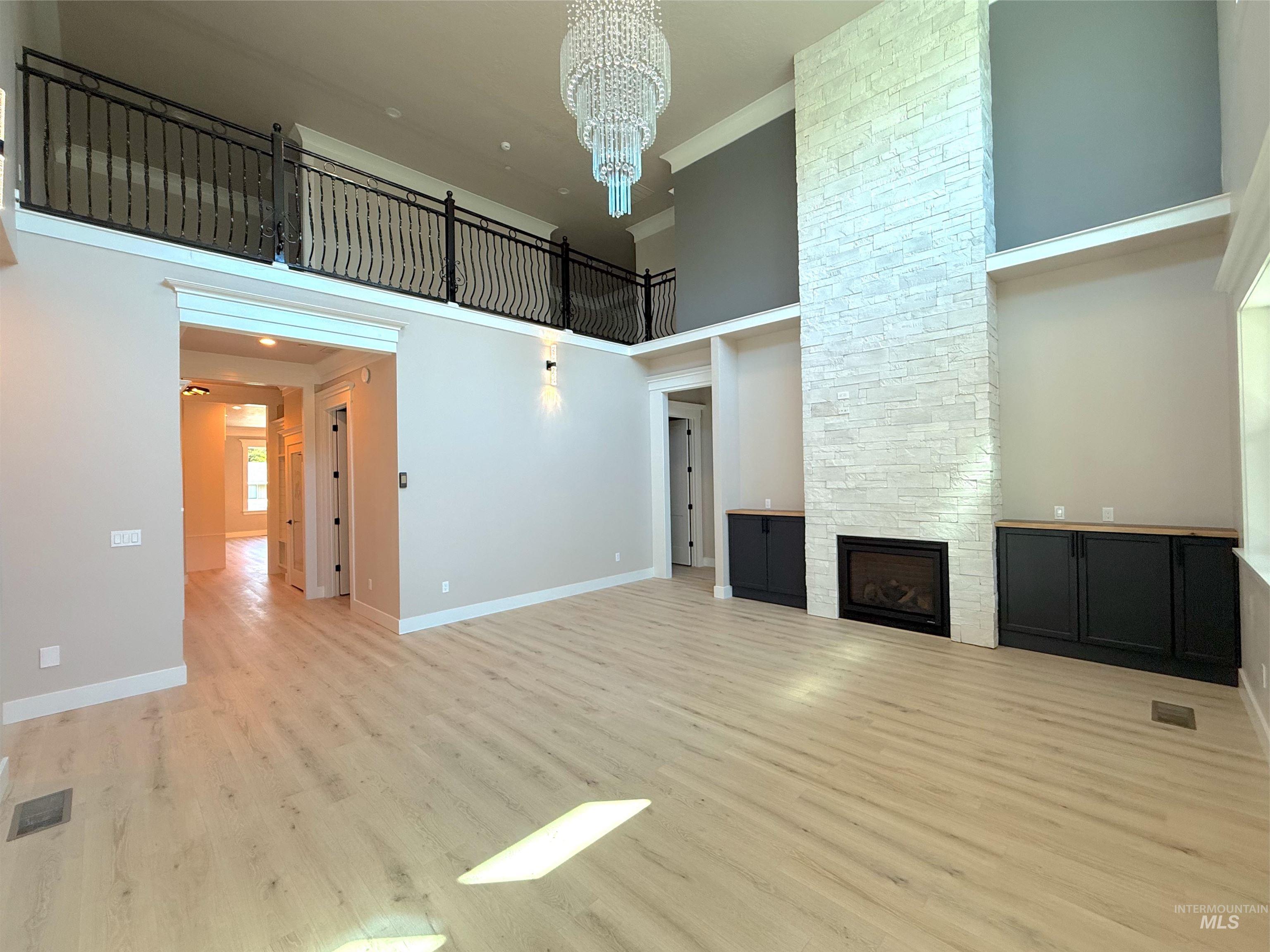 Unfurnished living room with a high ceiling, a fireplace, light wood-style floors, a chandelier, and ornamental molding