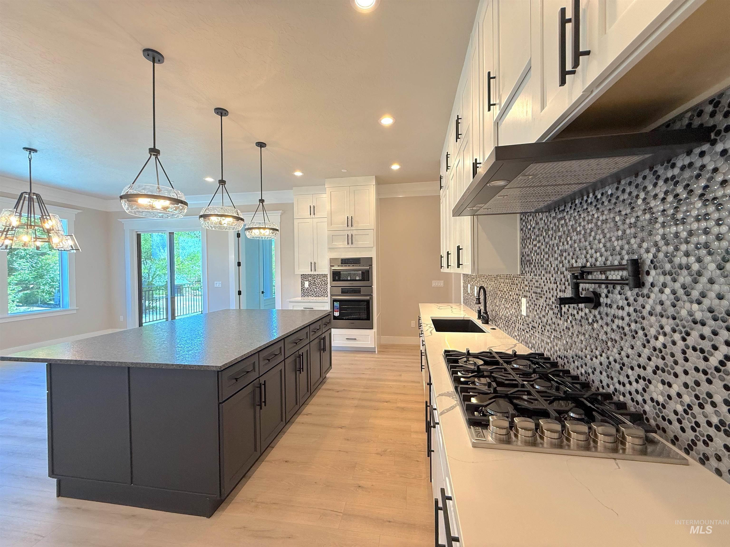 Kitchen with white cabinets, appliances with stainless steel finishes, decorative light fixtures, tasteful backsplash, and light wood-style floors