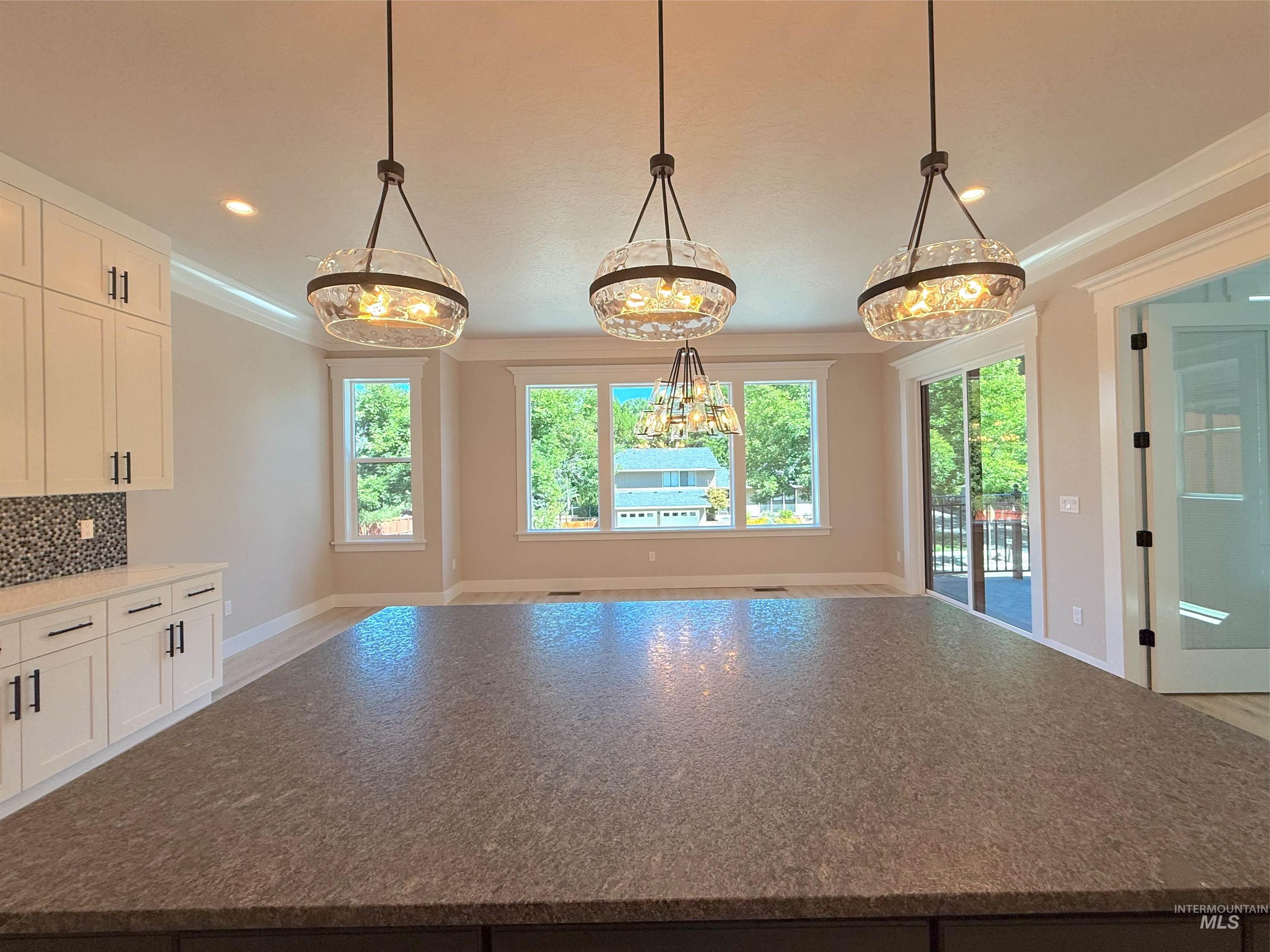 Kitchen with pendant lighting, dark stone countertops, white cabinetry, decorative backsplash, and healthy amount of natural light