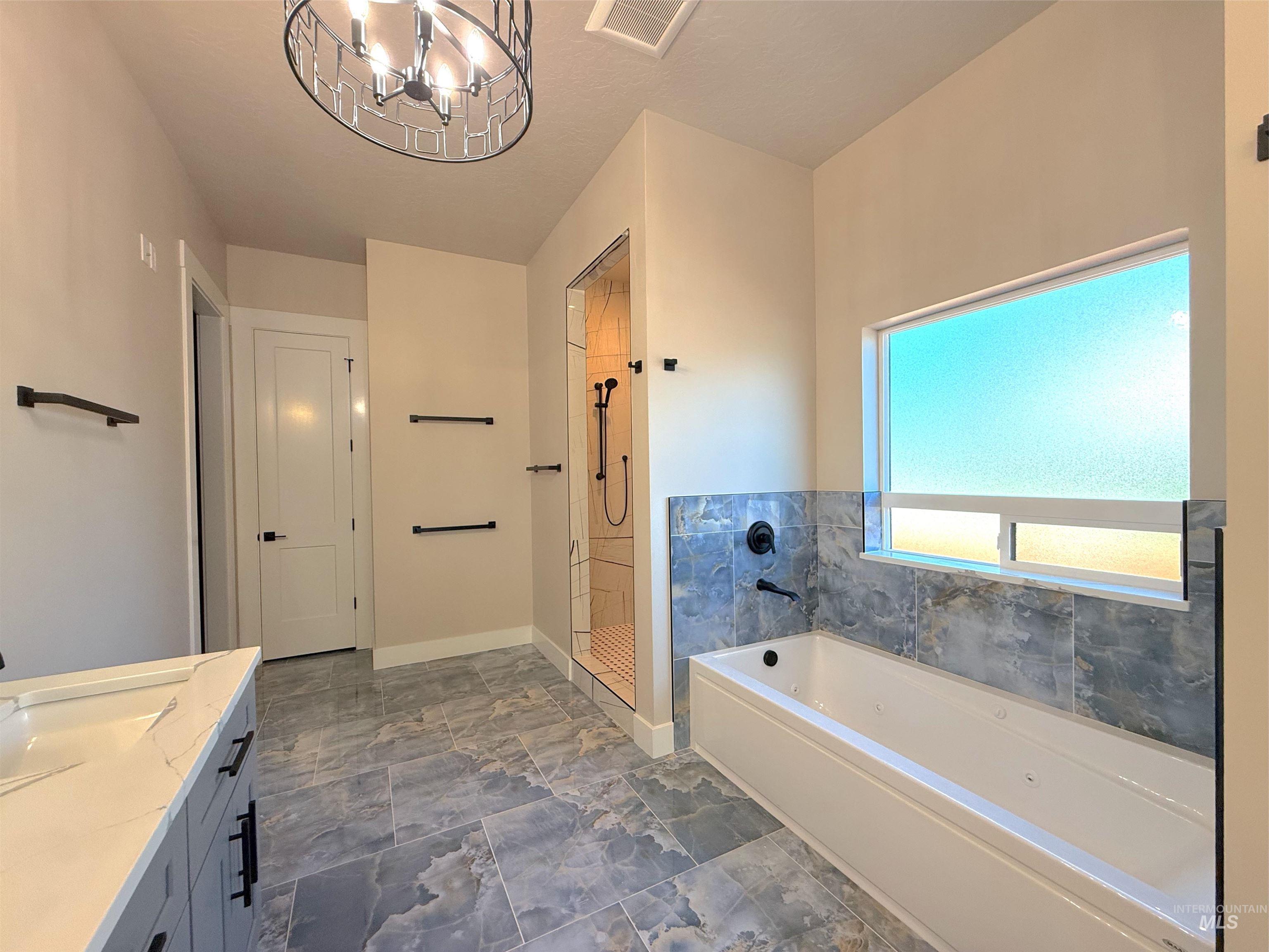 Full bath featuring a bath, vanity, a tile shower, and a chandelier