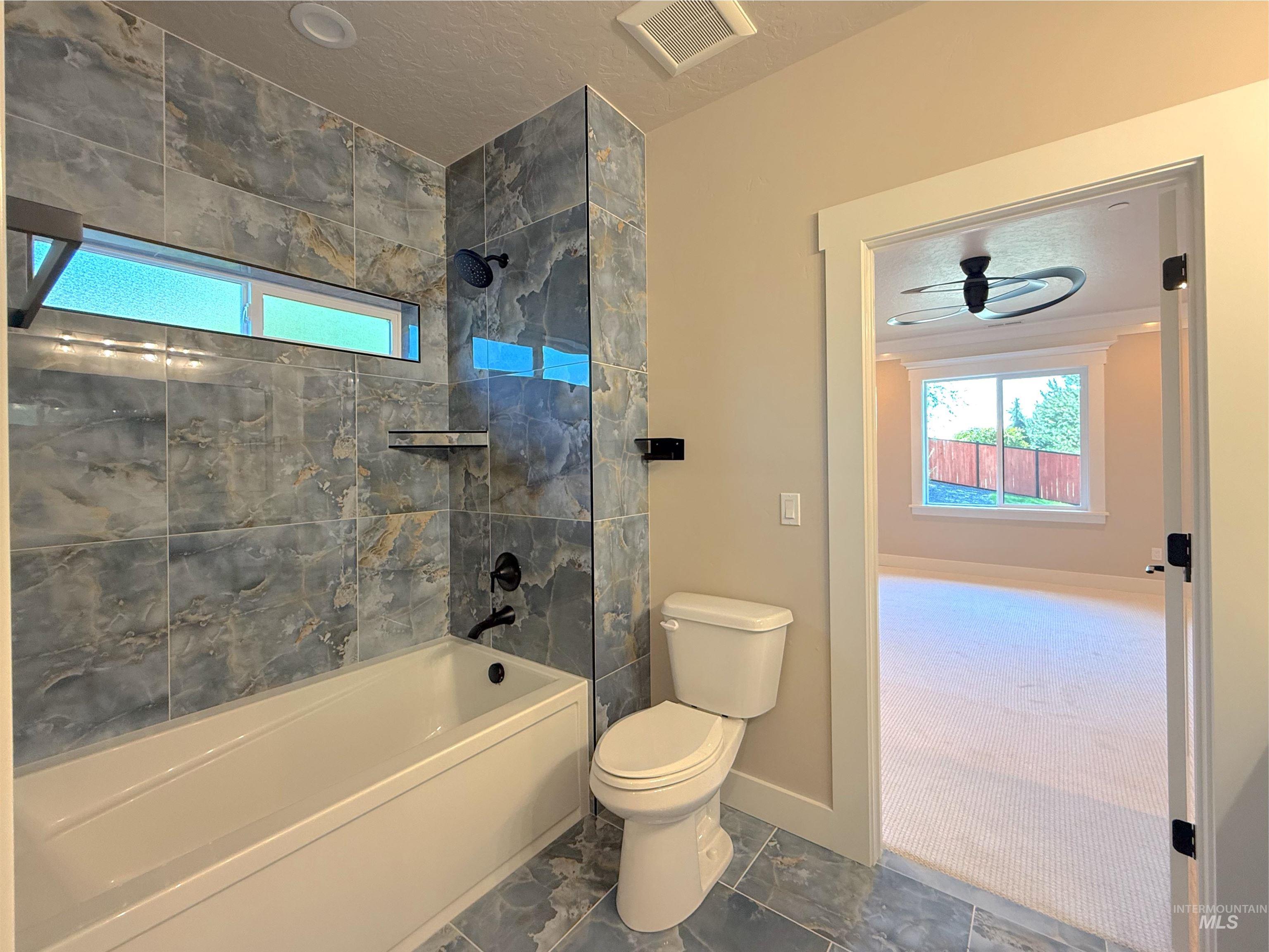 Bathroom featuring shower / tub combination, ceiling fan, and a textured ceiling