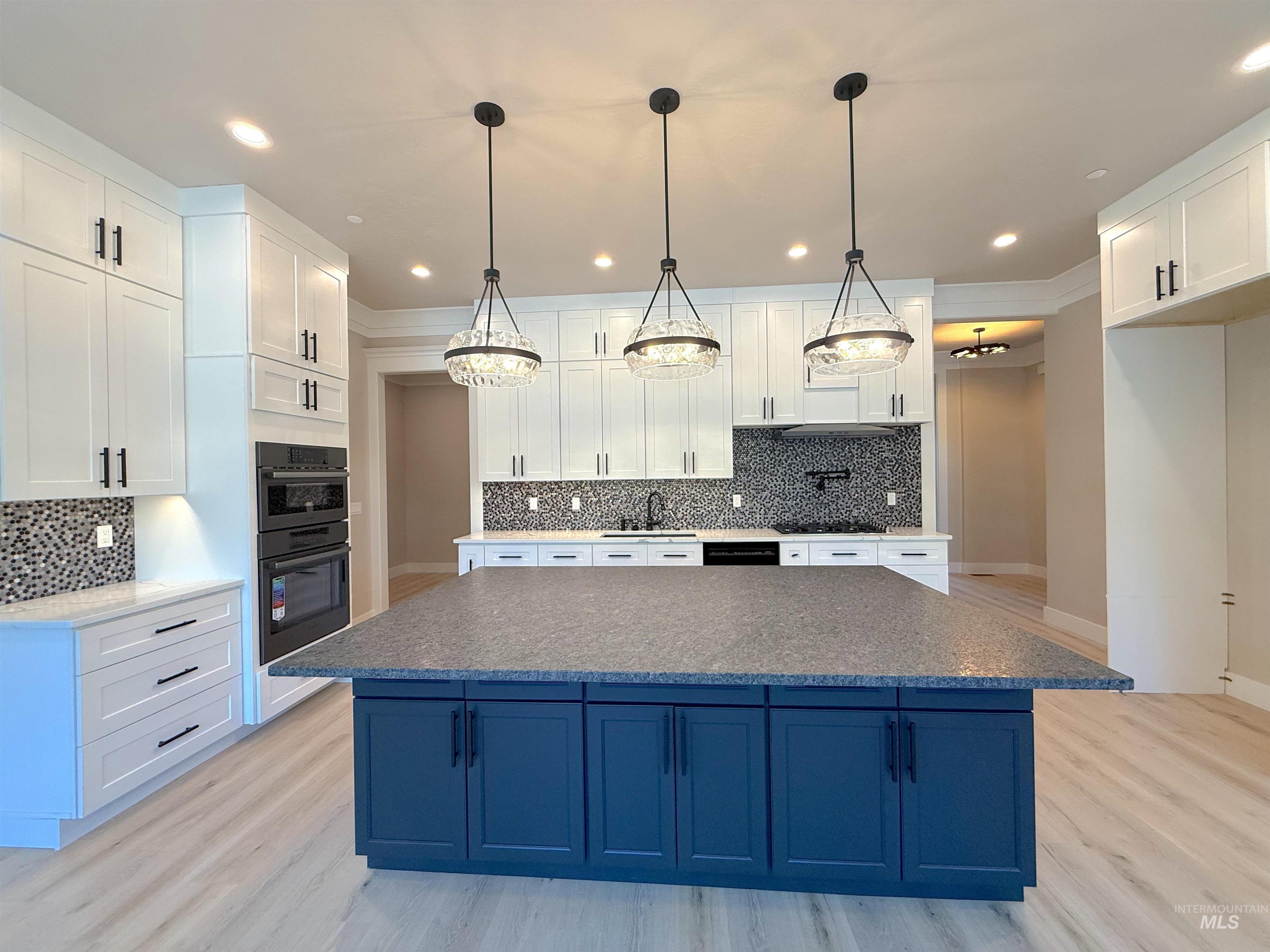 Kitchen featuring white cabinetry, tasteful backsplash, light wood-style floors, light stone countertops, and blue cabinets
