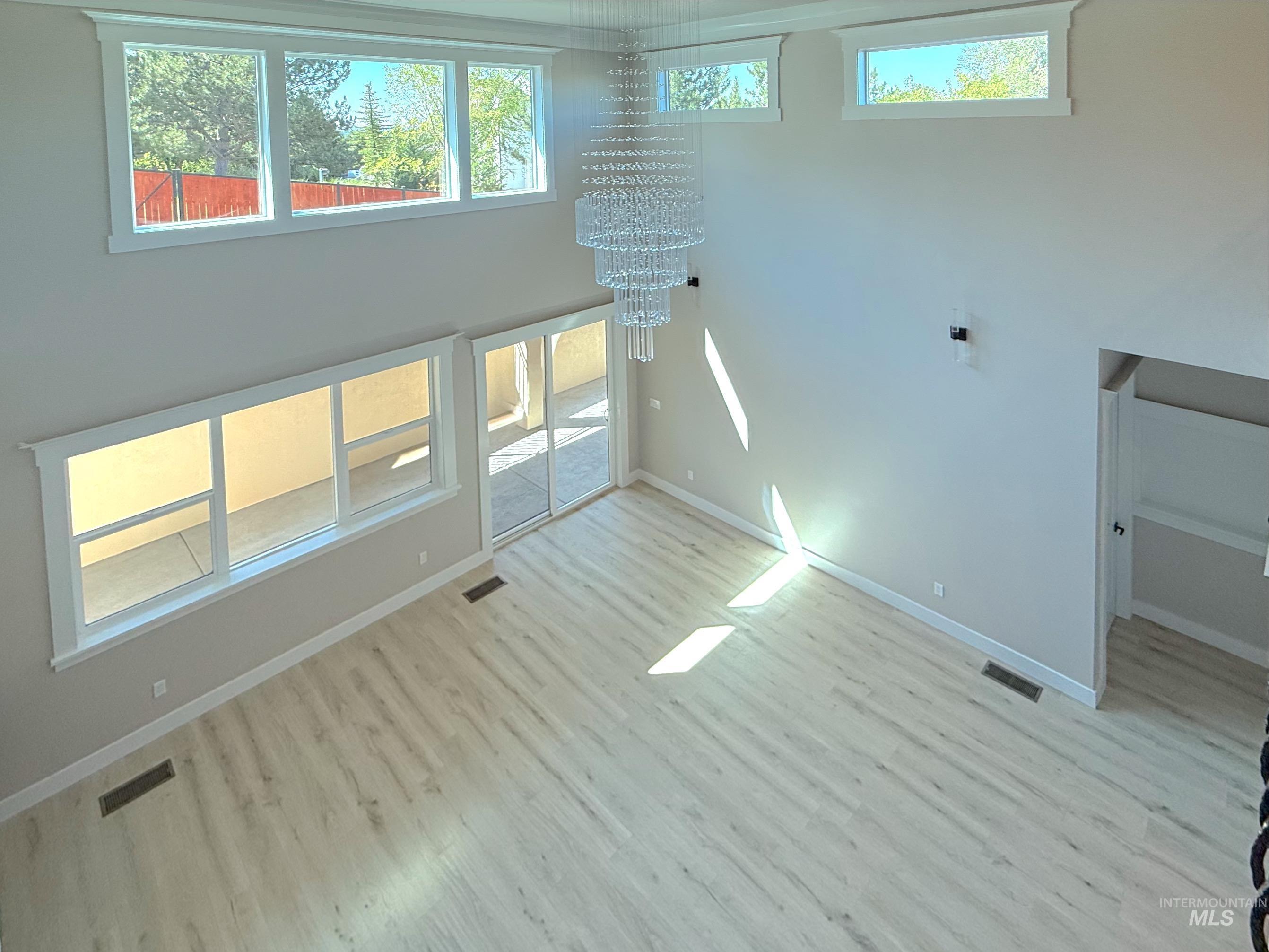 Unfurnished living room with a towering ceiling, light wood finished floors, and a chandelier