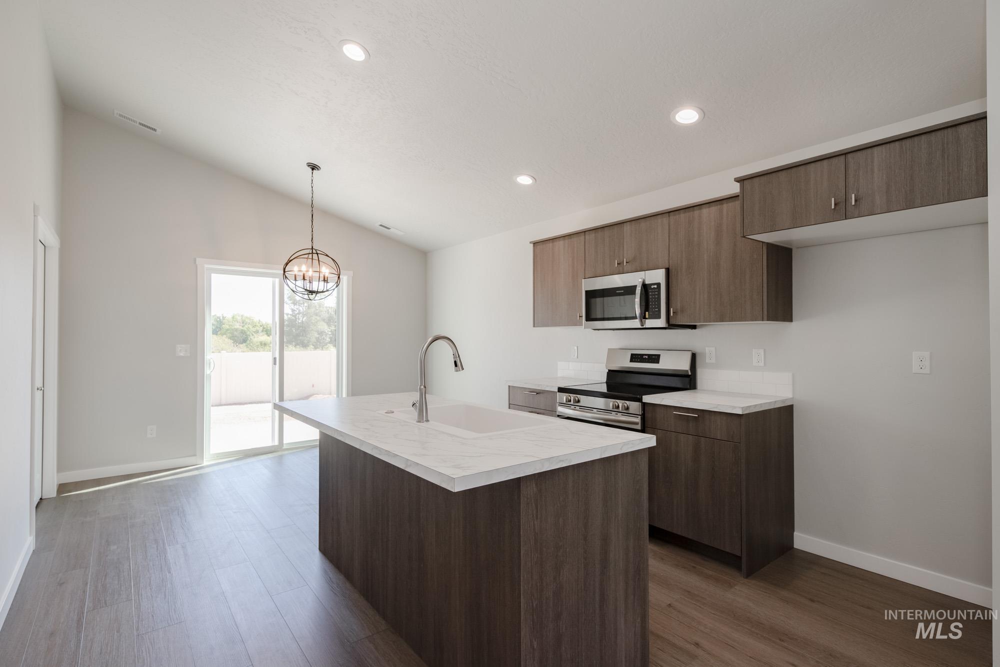 Kitchen with light countertops, vaulted ceiling, stainless steel appliances, decorative light fixtures, and a chandelier