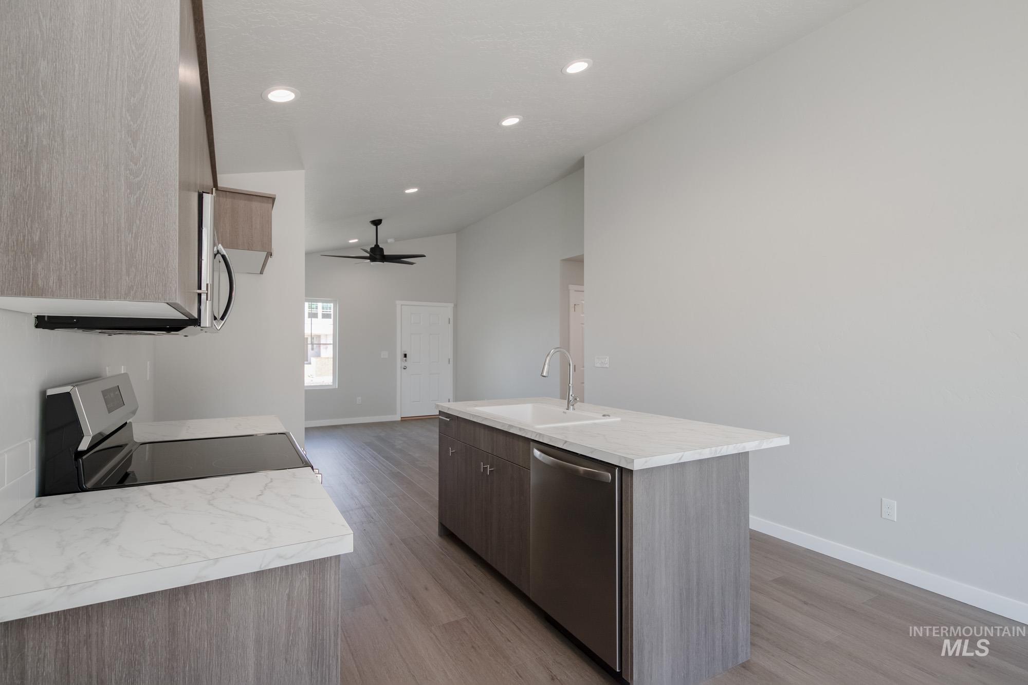 Kitchen featuring light countertops, an island with sink, appliances with stainless steel finishes, light wood finished floors, and lofted ceiling