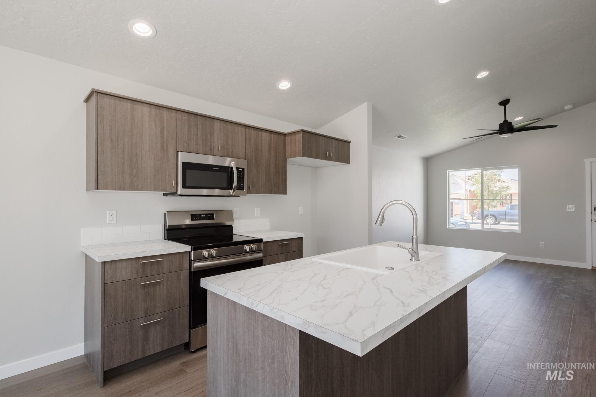 Kitchen with appliances with stainless steel finishes, light countertops, an island with sink, light wood finished floors, and a ceiling fan