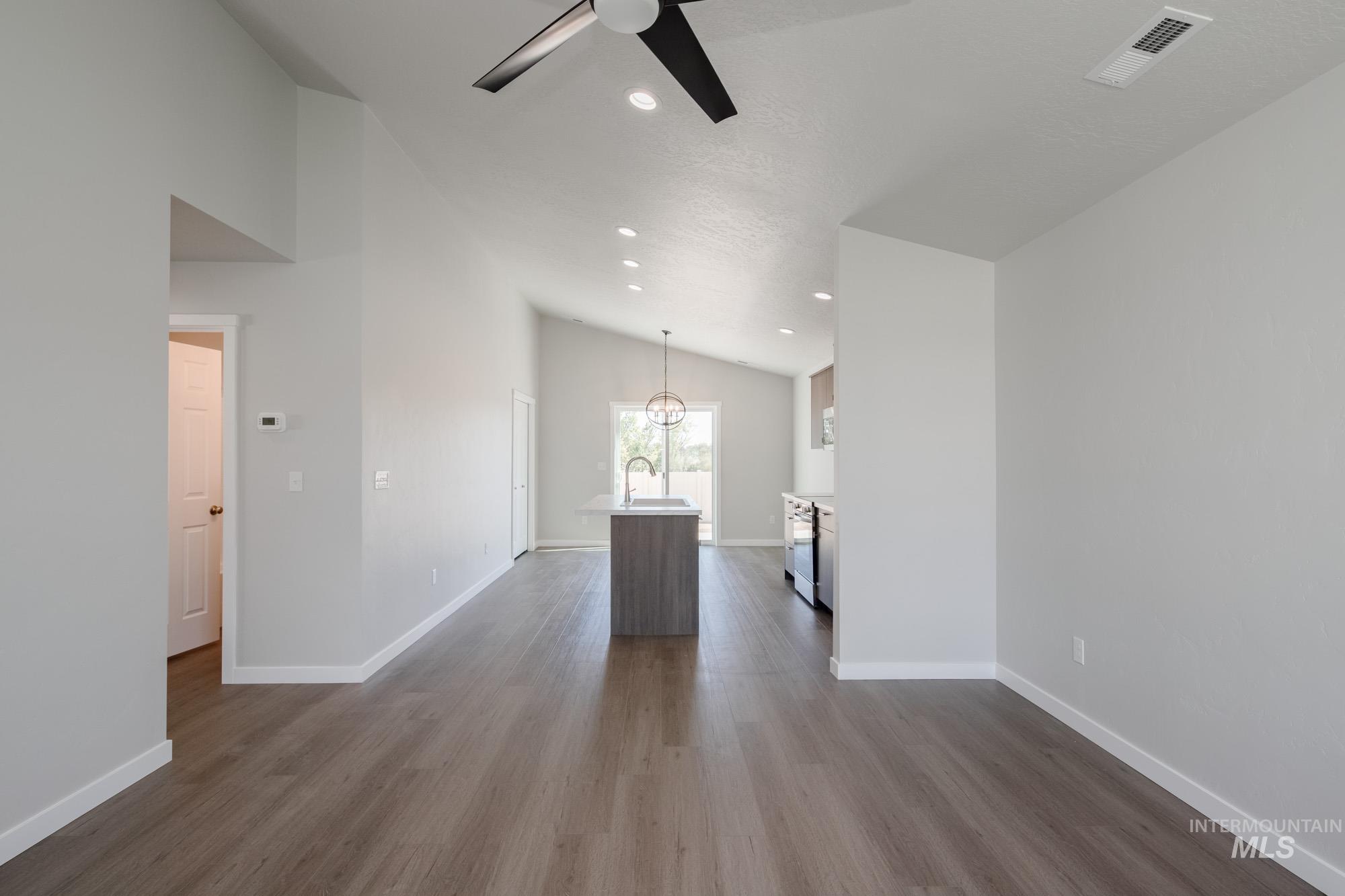 Unfurnished living room with dark wood-style flooring, recessed lighting, a ceiling fan, a chandelier, and high vaulted ceiling