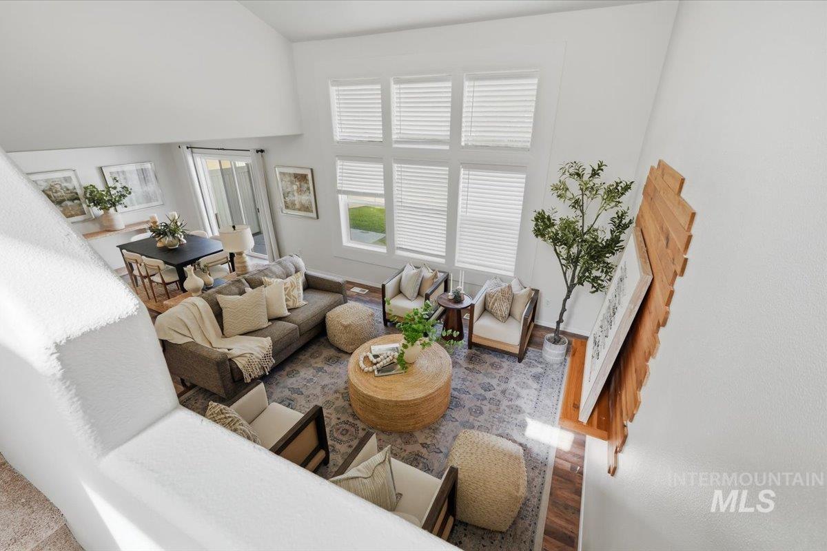 Two-story living area with high ceilings, multiple windows, wood-finish flooring, and an open concept layout with an adjacent dining area