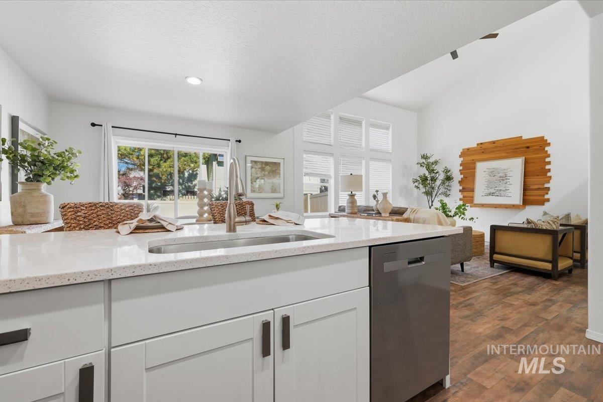 Kitchen island featuring a stainless steel undermount sink, quartz countertop, and white shaker-style cabinetry with dark hardware