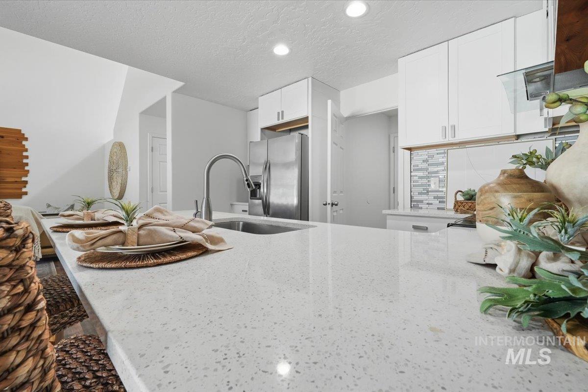 Spacious kitchen island with light speckled countertop, undermount stainless steel sink, gooseneck faucet, white cabinetry, and mosaic tile backsplash