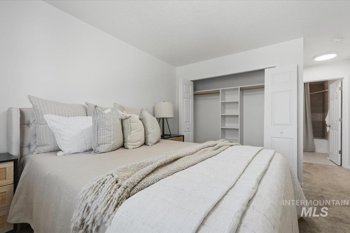 Bedroom featuring a built-in closet with bifold doors and shelving, textured carpet flooring, and a doorway to an adjacent bathroom with a tub/shower combination