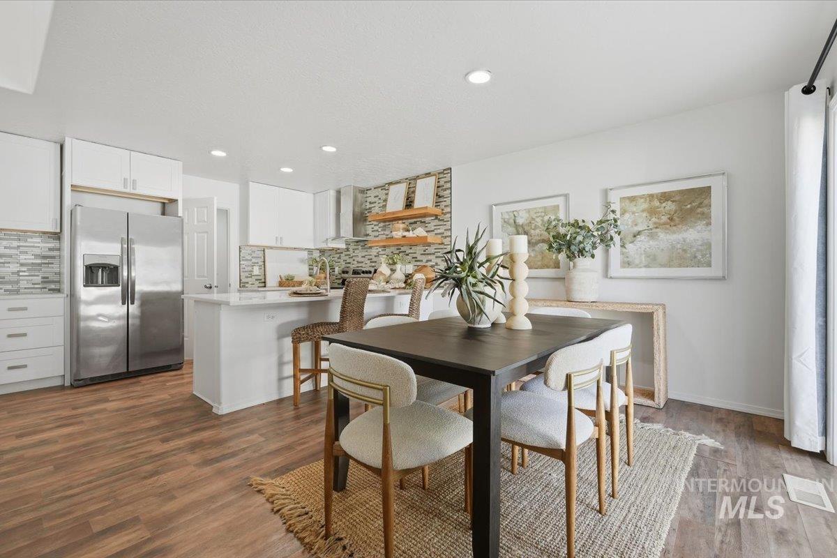Open-concept kitchen and dining area featuring wood-finish flooring, white cabinetry, a large kitchen island with seating, a mosaic tile backsplash, and recessed lighting