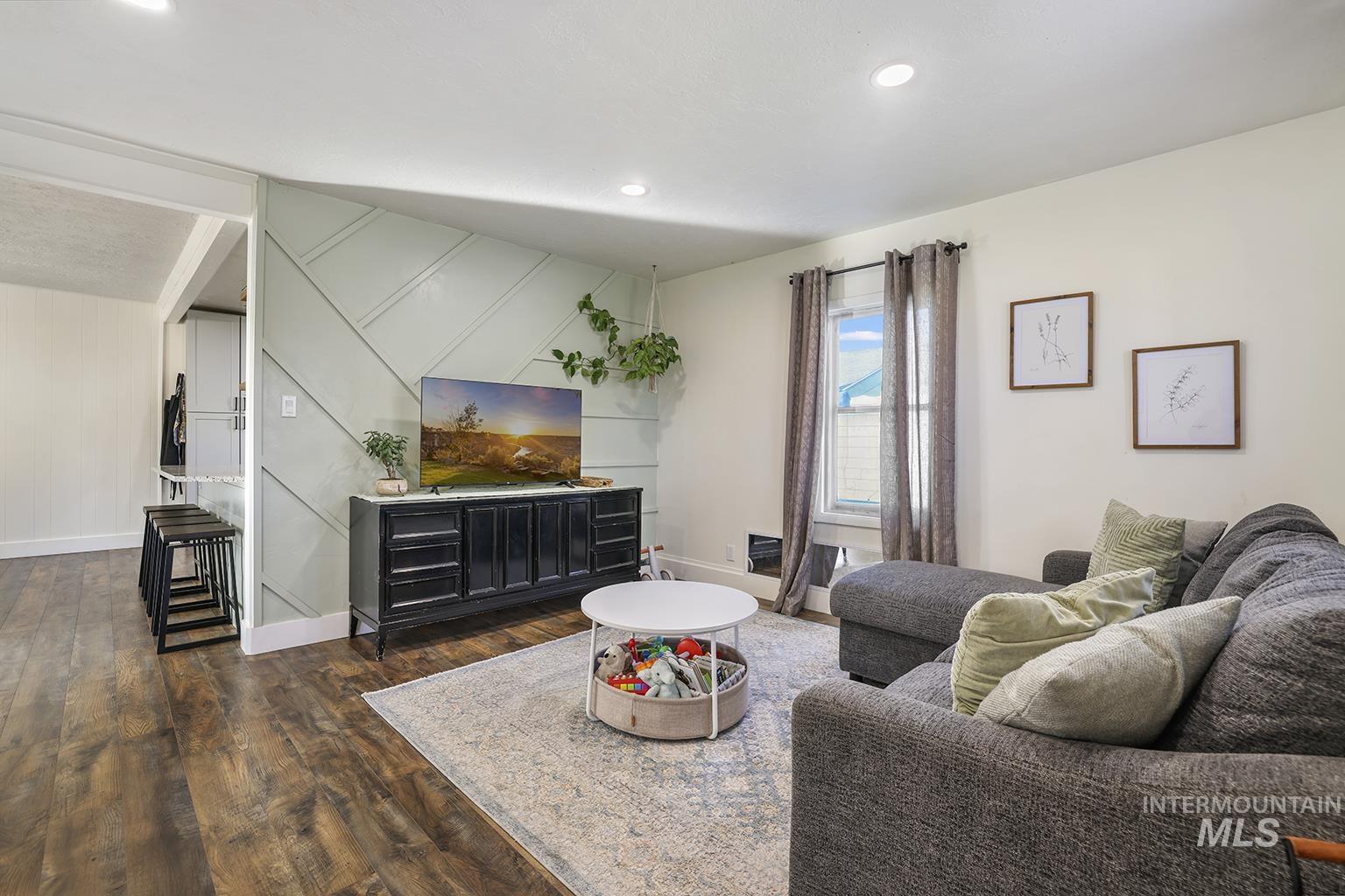 Living room featuring dark wood finished floors, recessed lighting, and a decorative wall