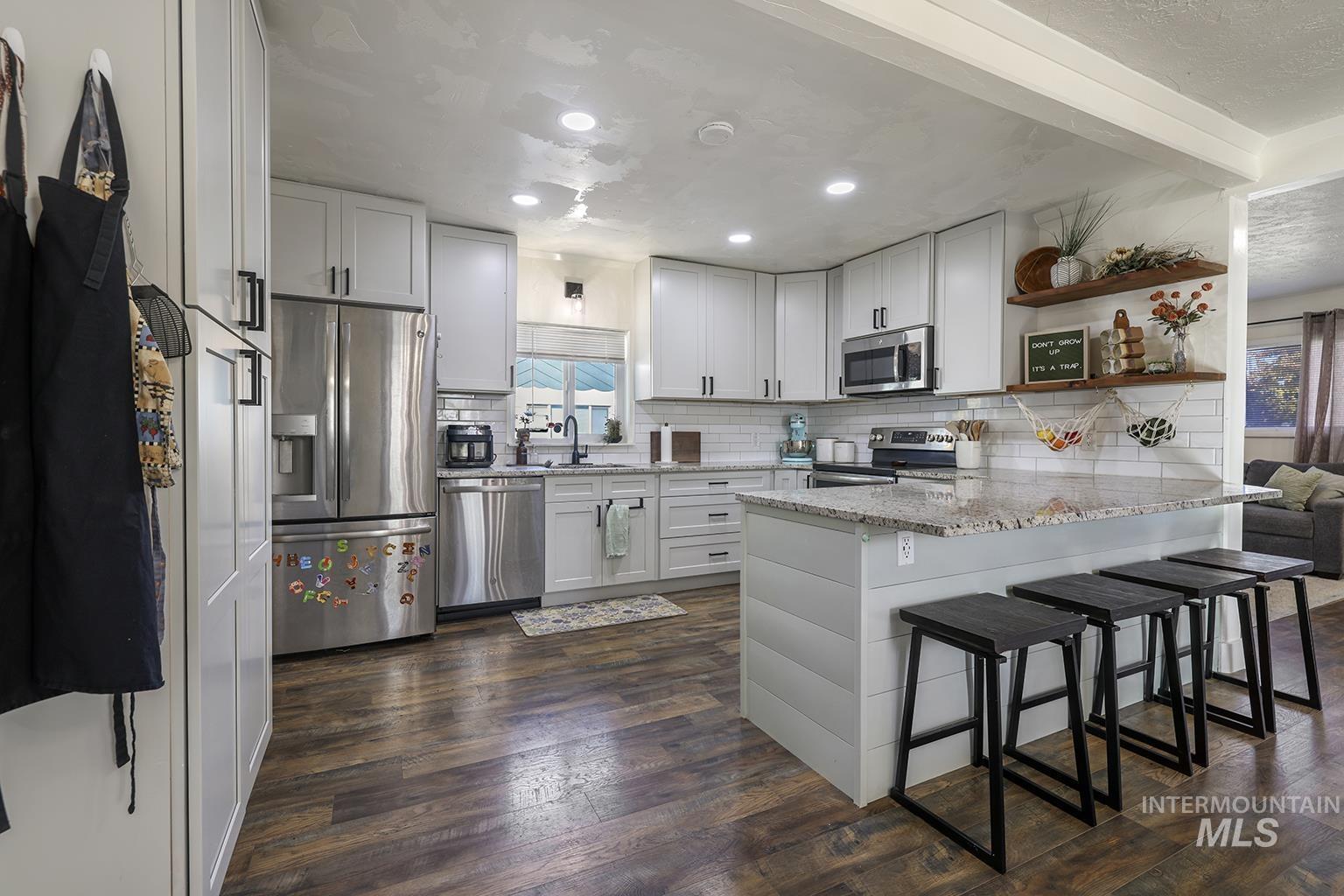 Kitchen featuring light stone countertops, tasteful backsplash, appliances with stainless steel finishes, open shelves, and a peninsula