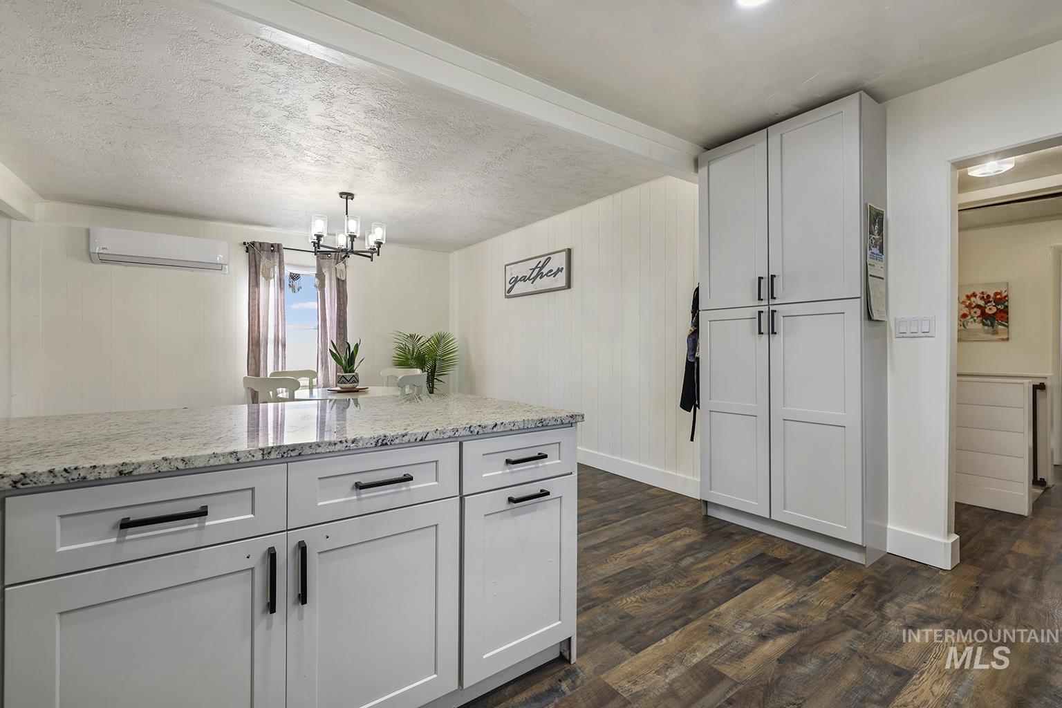 Kitchen with light stone countertops, dark wood-style floors, a textured ceiling, pendant lighting, and a chandelier
